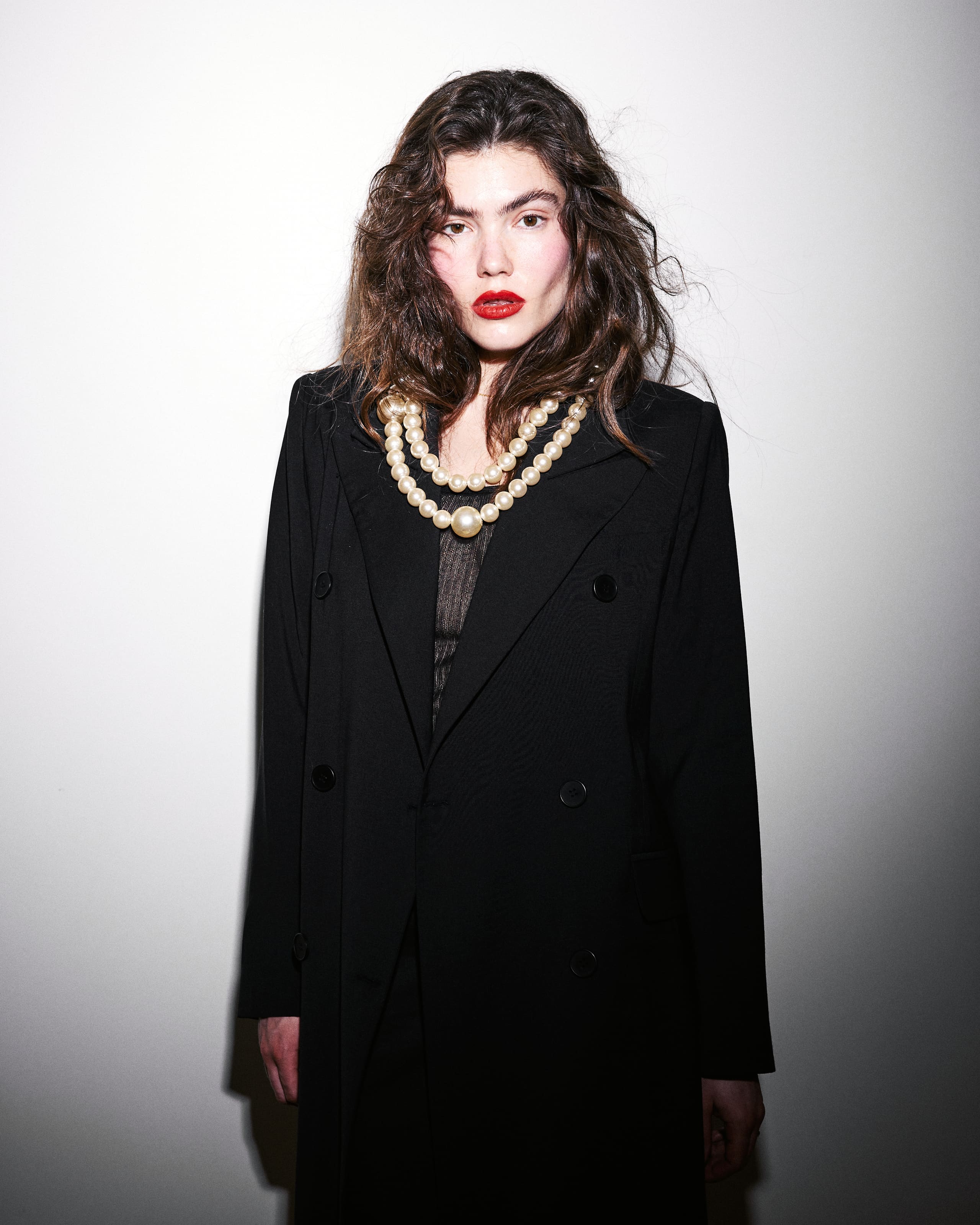 A step back from the pearls, AGIC's black double-breasted coat squares up under tangled waves and red lips.