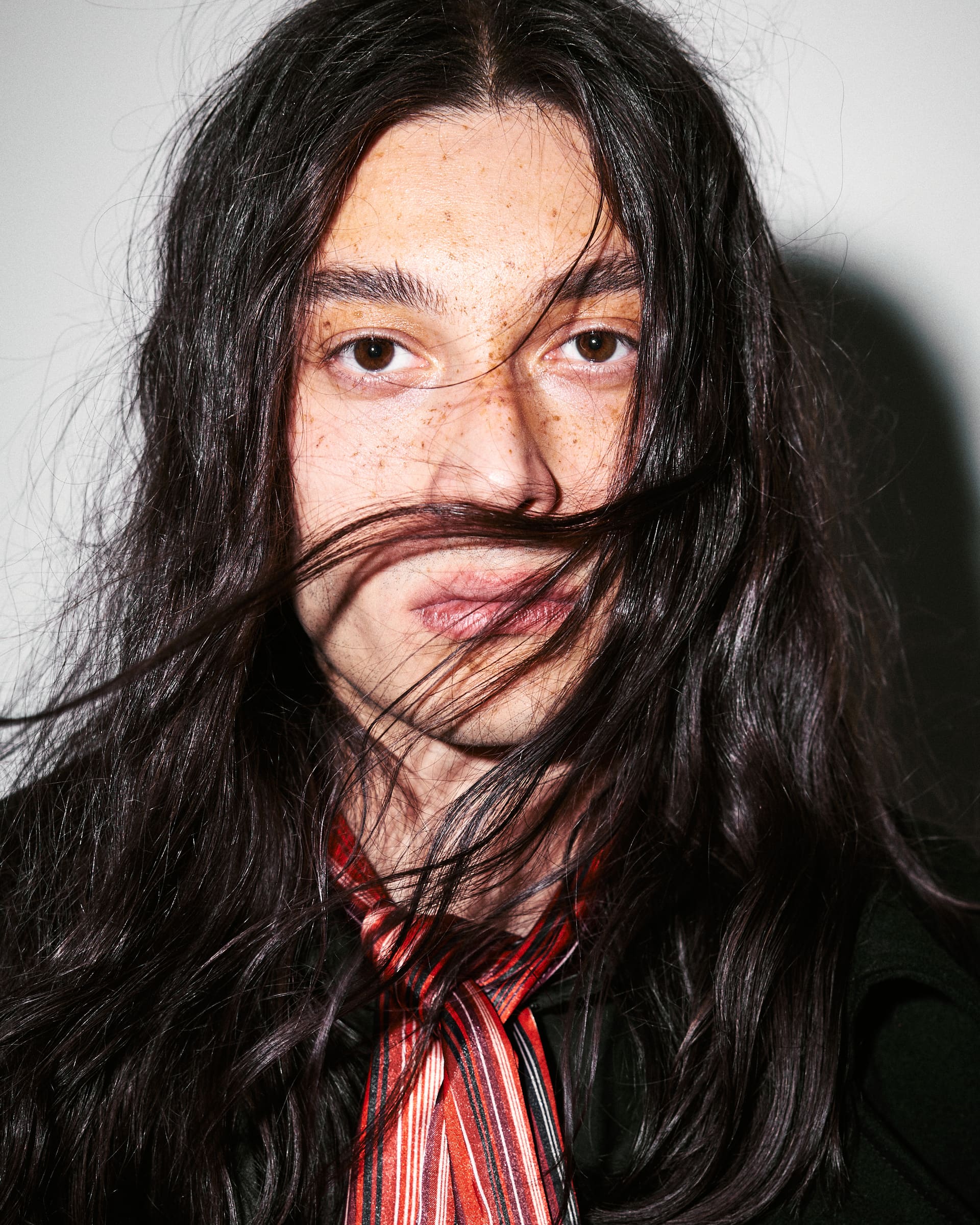 Loose black hair sweeps across a freckled face above AGIC's striped crimson scarf.