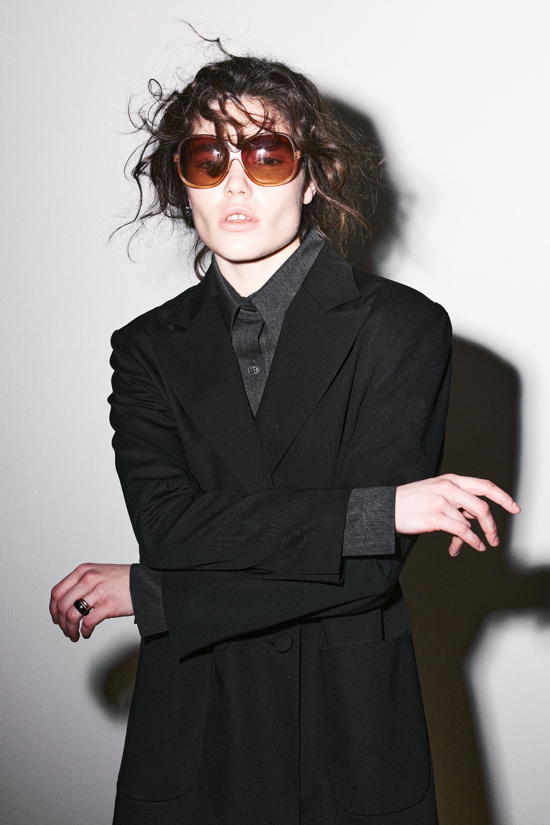 Amber seventies sunglasses and gestural hands loosen AGIC's sharp black tailoring.