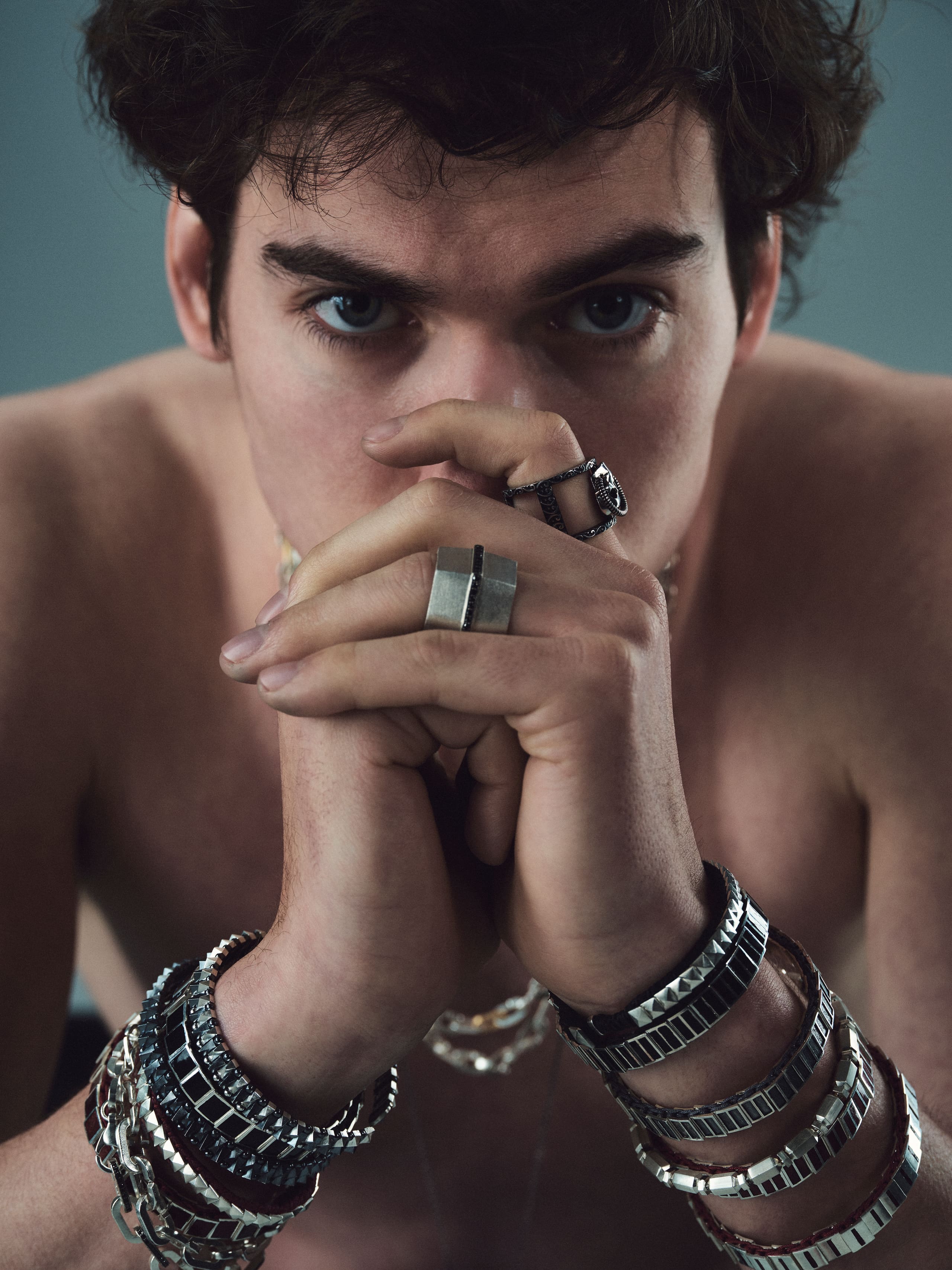 Stacked silver bracelets and sculptural rings frame a direct gaze in the Dime Tribe studio.