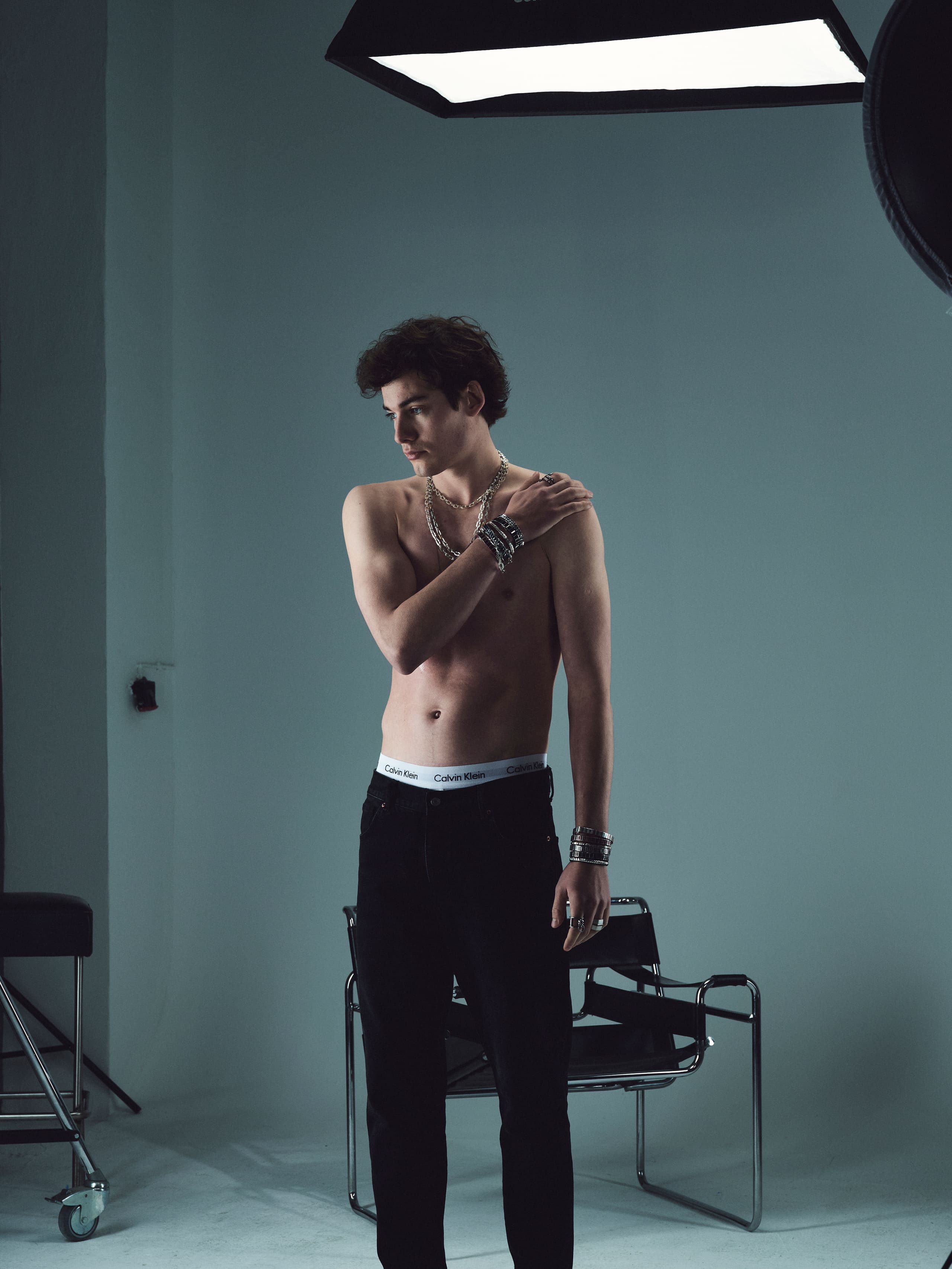 A full-length figure in black denim and layered Dime Tribe chains stands between the studio softboxes.