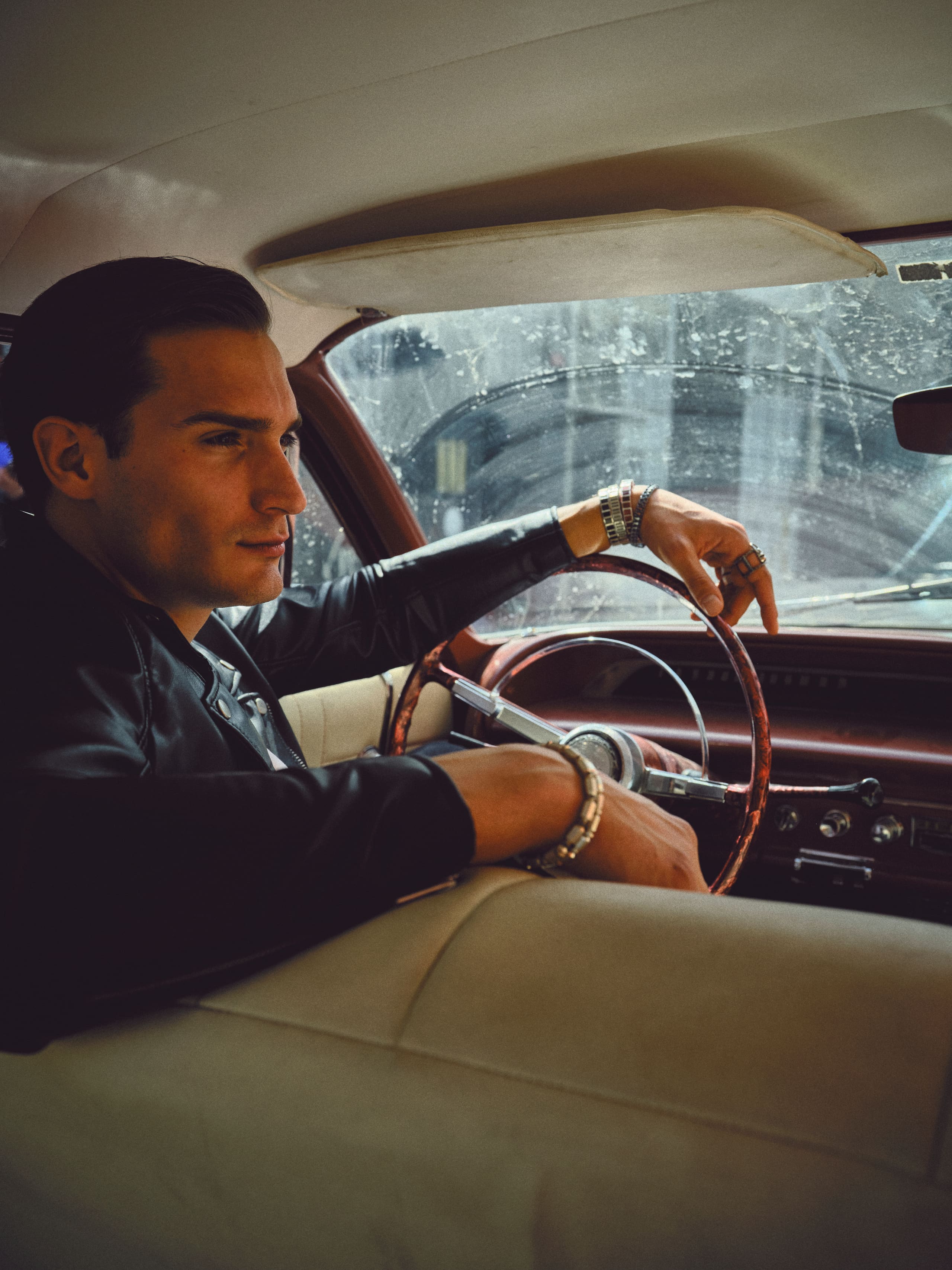 Slicked back in a leather jacket at the wheel of a classic sedan, wrists lined with Dime Tribe silver.