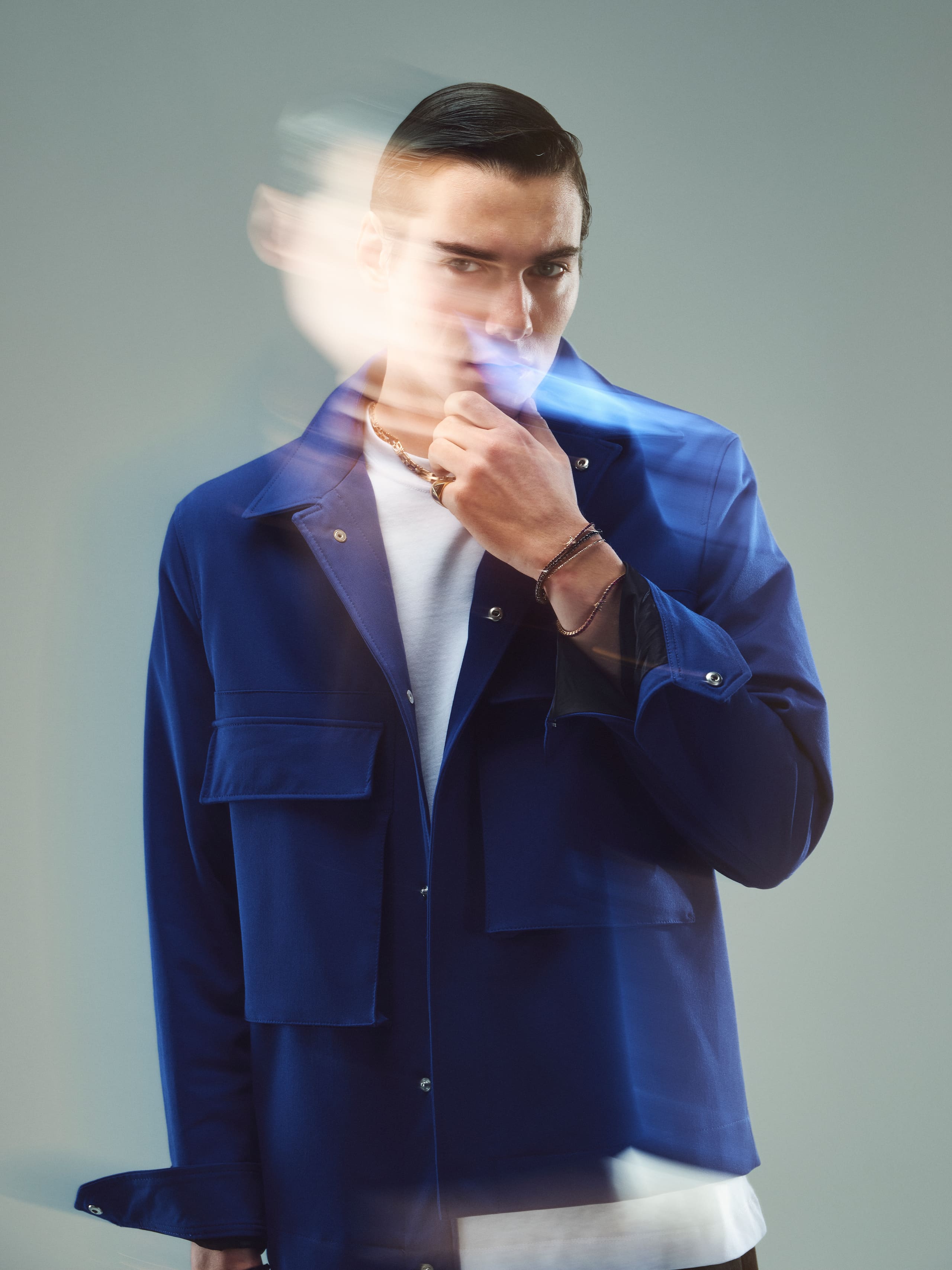 A streak of motion blurs the face while gold Dime Tribe chains hold sharp against workwear blue.