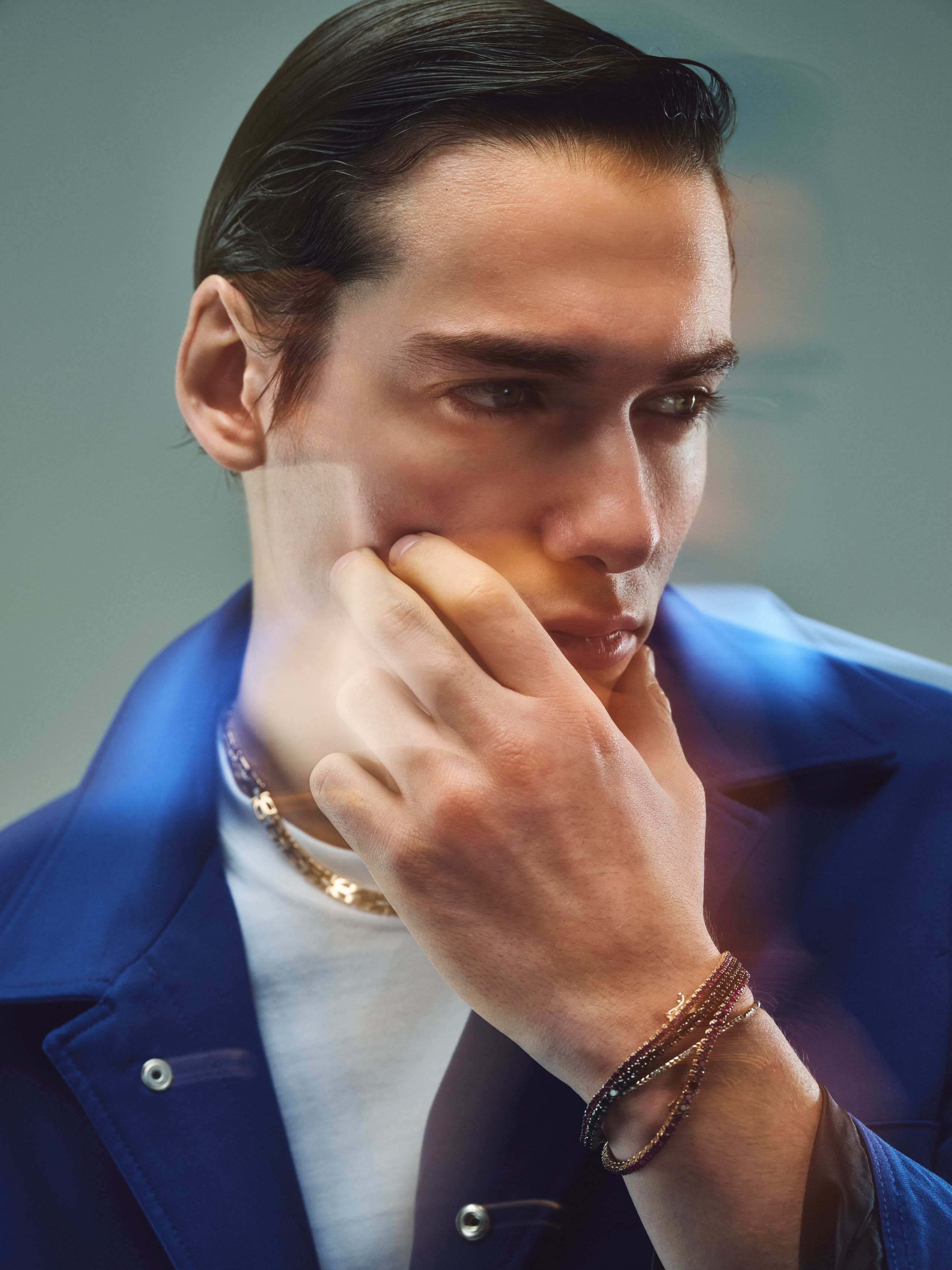 A gold curb chain and beaded Dime Tribe bracelets in a soft-focus cobalt-jacket portrait.
