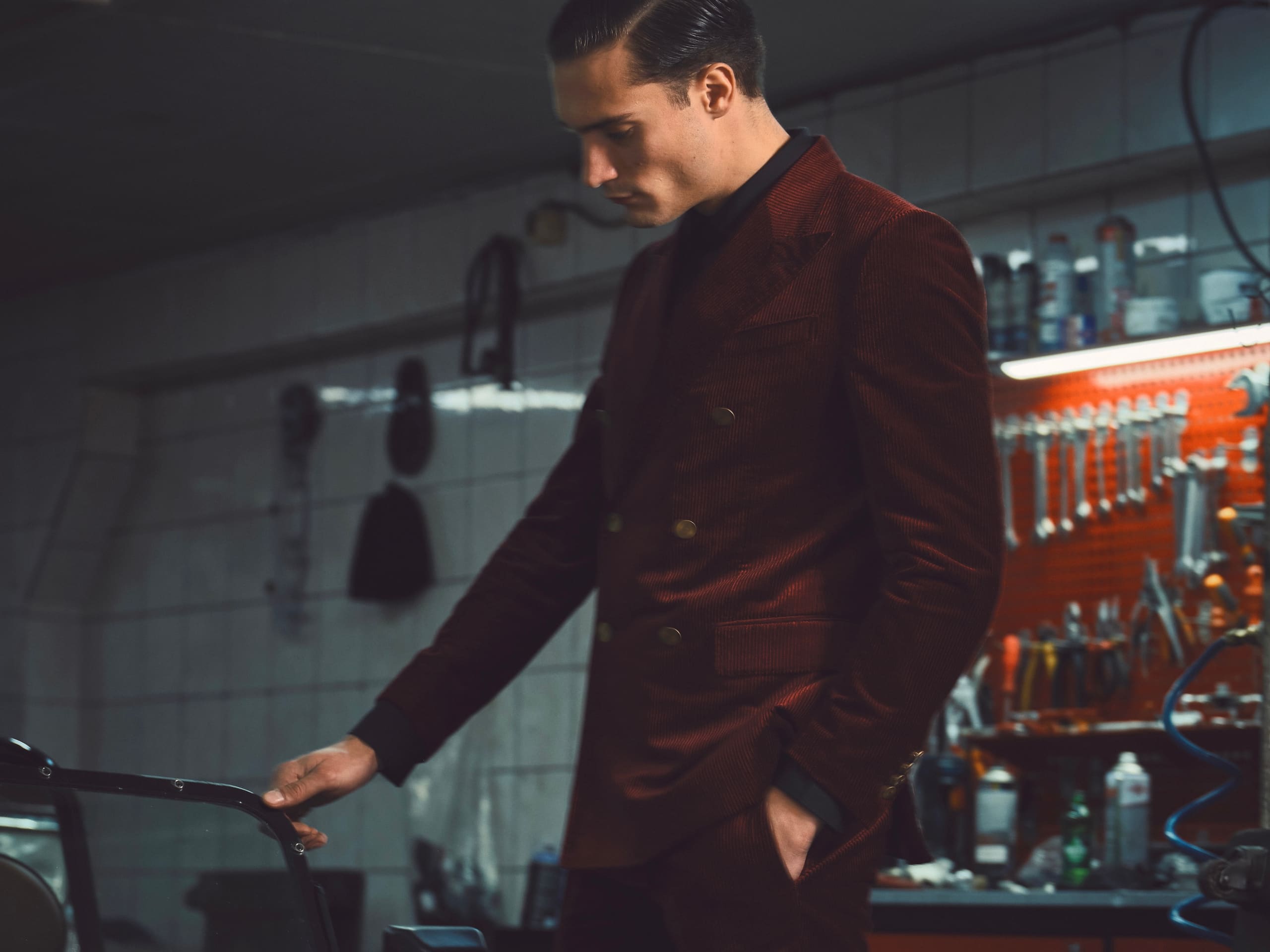 A double-breasted burgundy corduroy suit among the wrenches of a mechanic's workshop for Dime Tribe.
