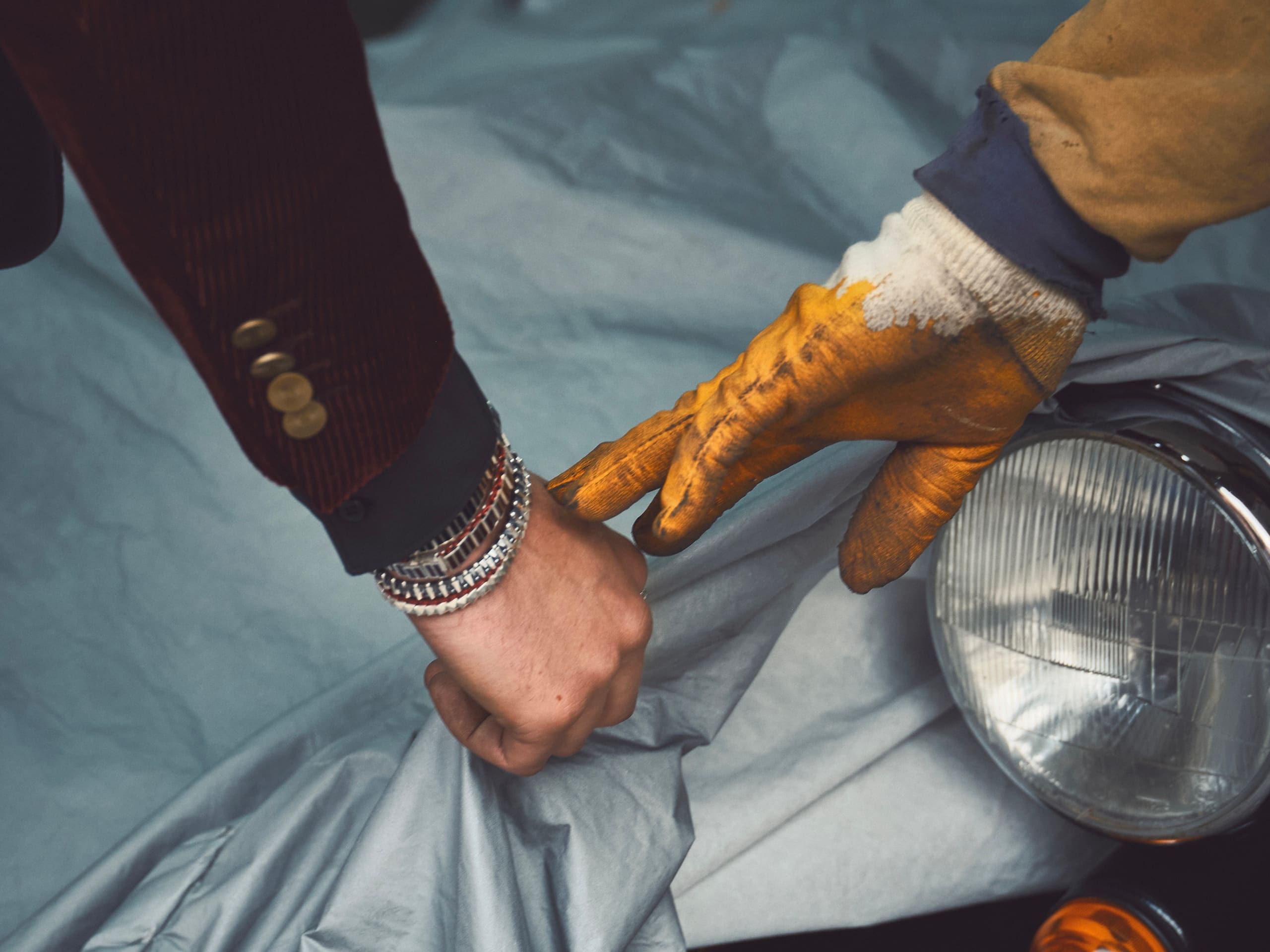 A jewelled wrist meets a mechanic's glove over the covered headlamp of a classic roadster for Dime Tribe.
