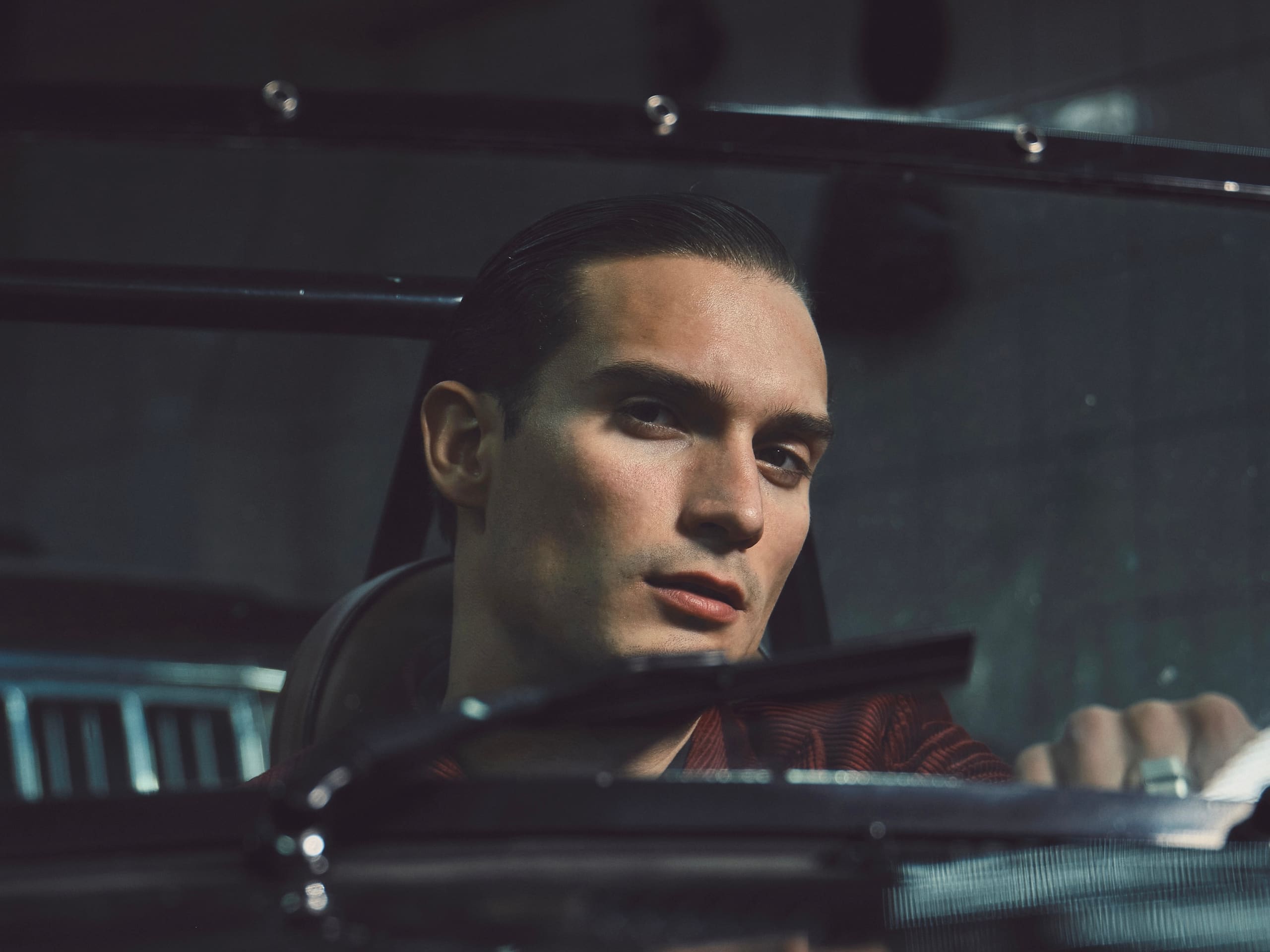 Closer through the split windshield, the driver's gaze stays level while a Dime Tribe ring catches the garage light on the wheel.