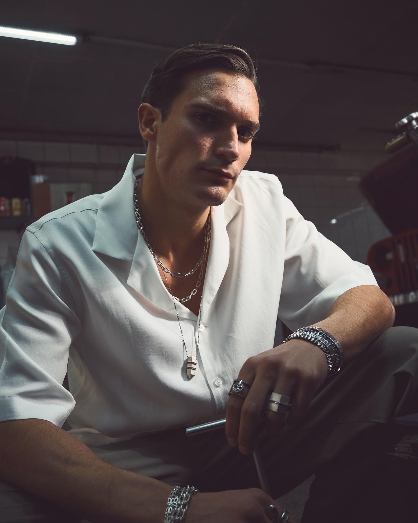 Layered Dime Tribe chains and signet rings meet a direct gaze in the half-light of the workshop.