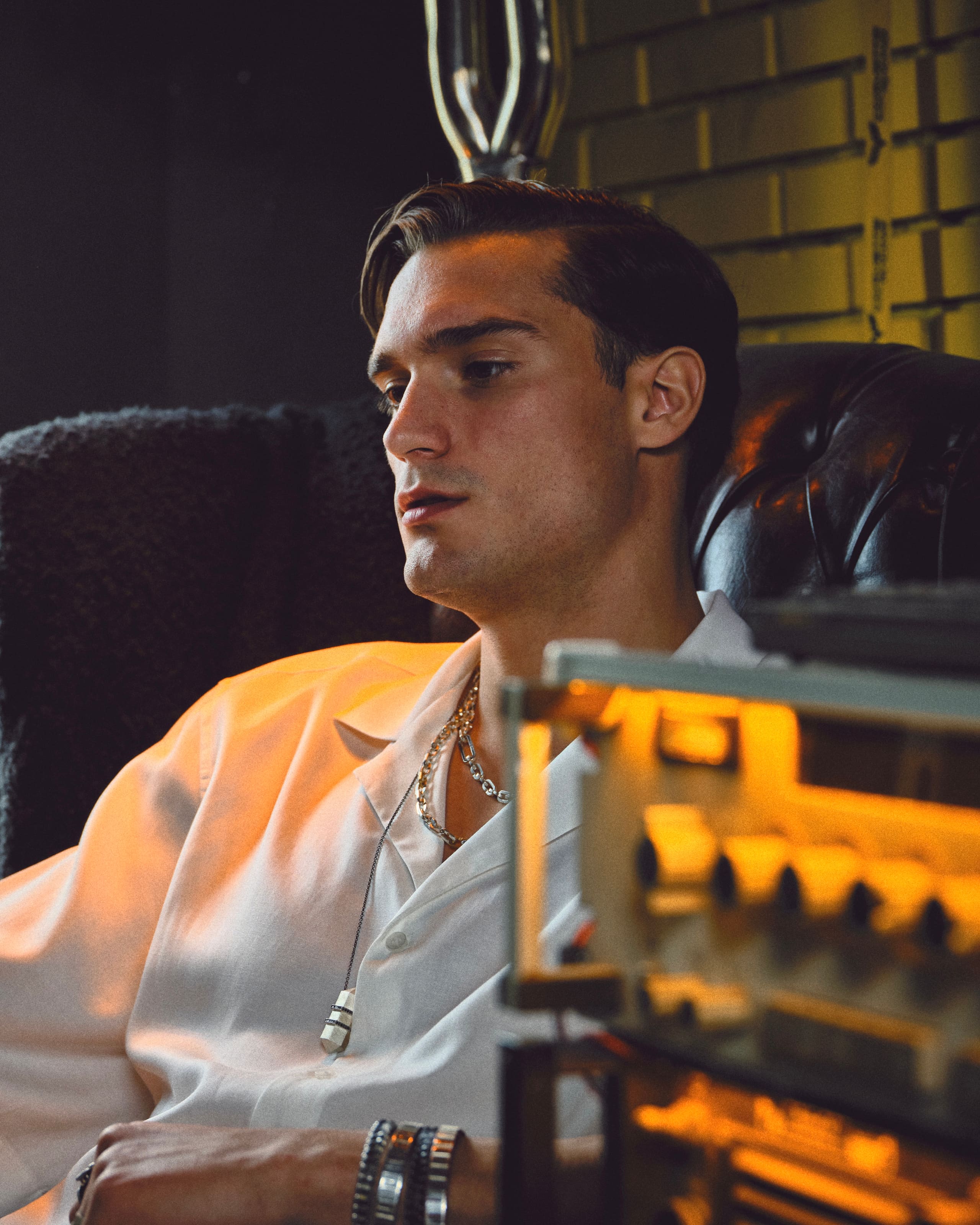 Beside the glowing dials of an old radio, the model's Dime Tribe chains and pendant slip into the half-shadow of the armchair.