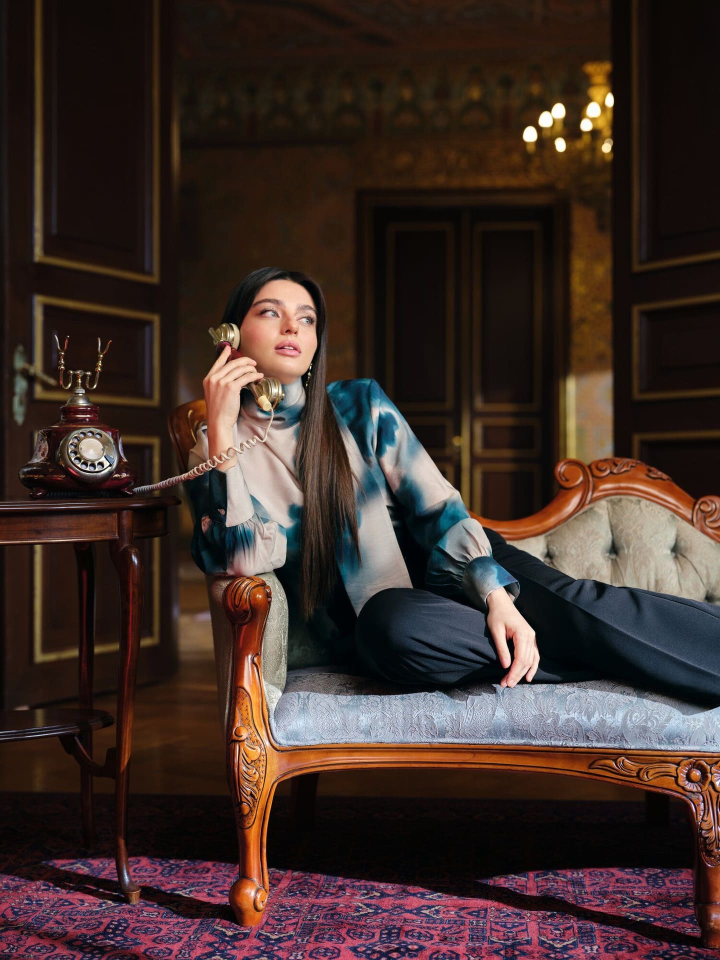 Ayça Ayşin Turan takes a call on a vintage rotary phone from a carved chaise longue in a palatial Istanbul interior for LC Waikiki.