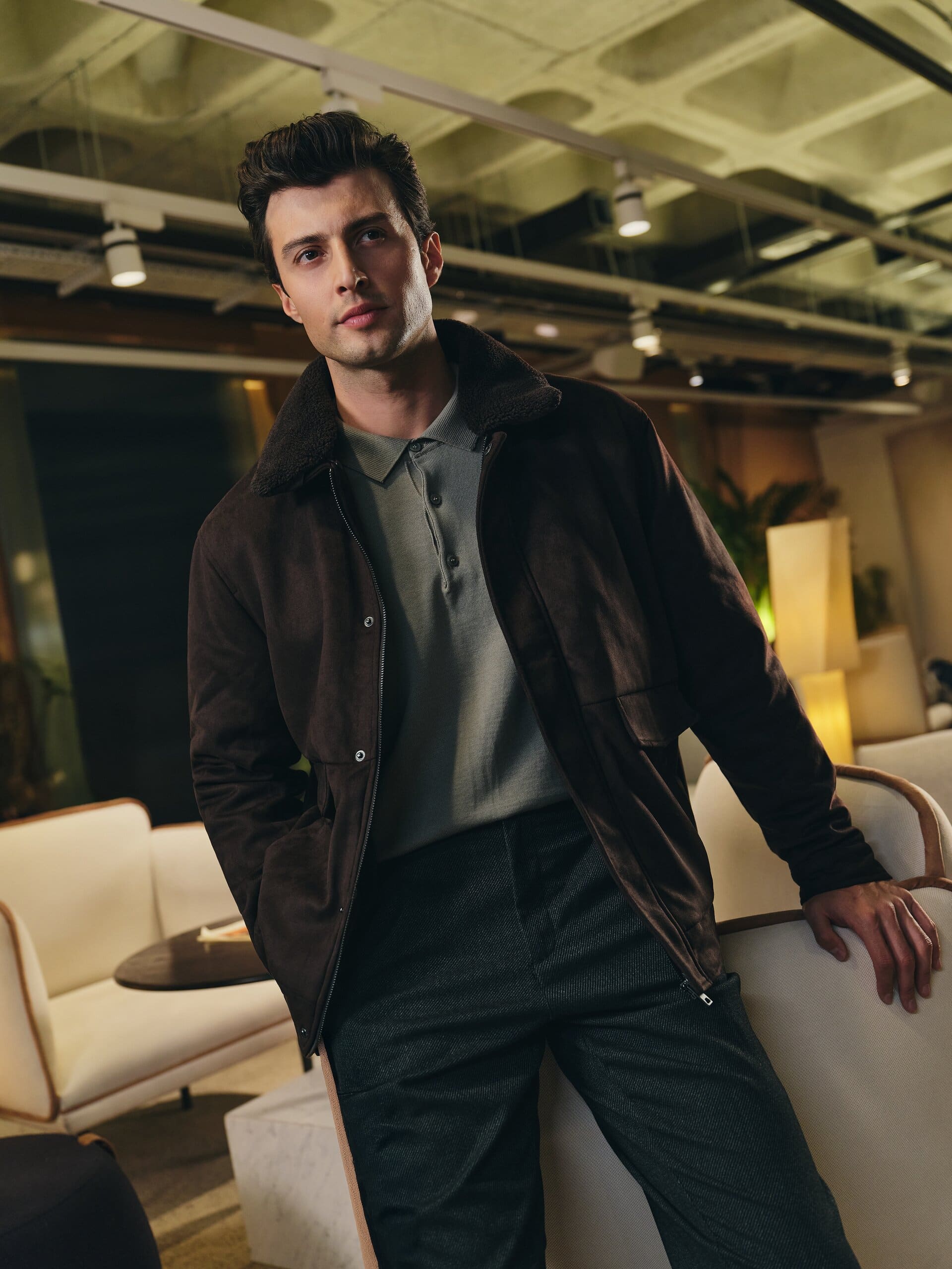 A shearling-collared brown jacket over a sage polo catches the lamplight of an after-hours lounge for LC Waikiki