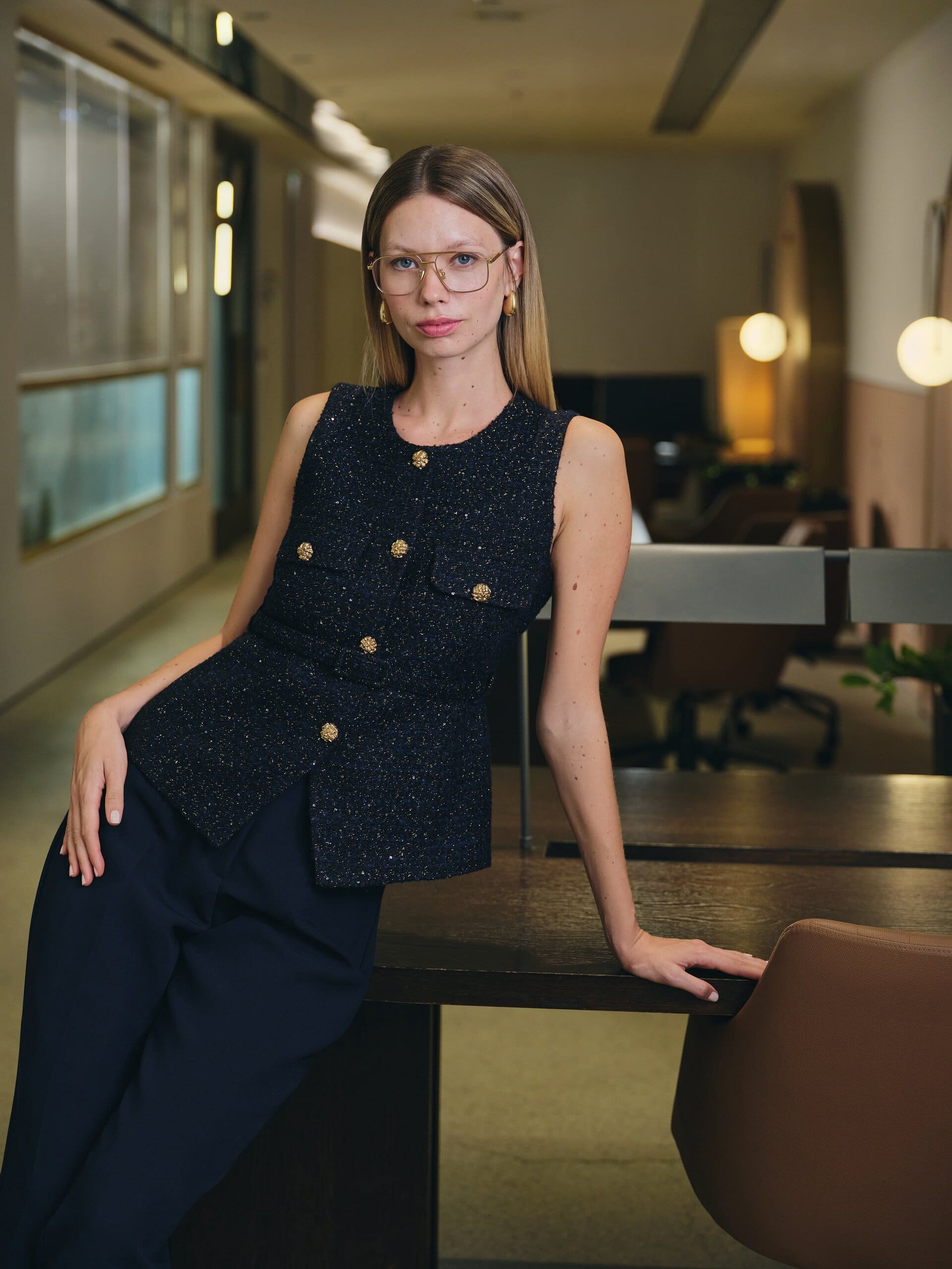 A sparkling navy tweed vest with gold buttons anchors a poised pose across an empty office desk for LC Waikiki