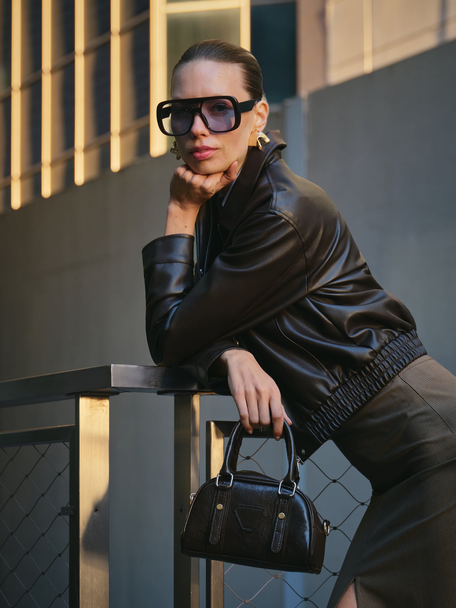 Golden-hour light rakes a dark leather bomber as a model props her chin on her fist, mini bowler bag in hand, for LC Waikiki