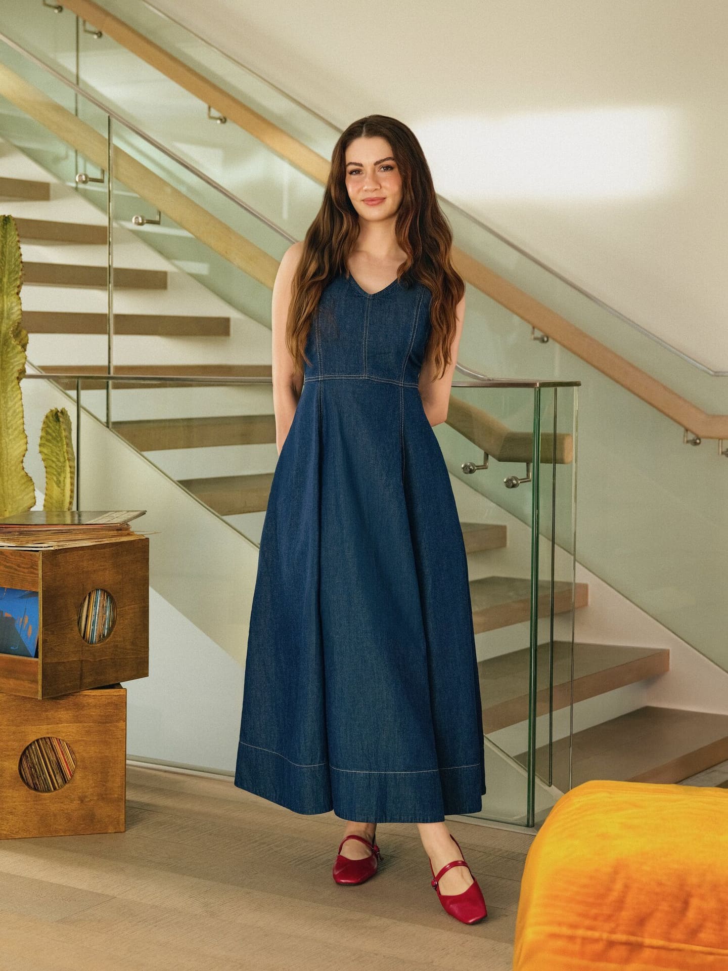 Burcu Özberk closes the spring story in a flared denim maxi dress and red Mary Janes at the foot of a glass staircase for LC Waikiki.
