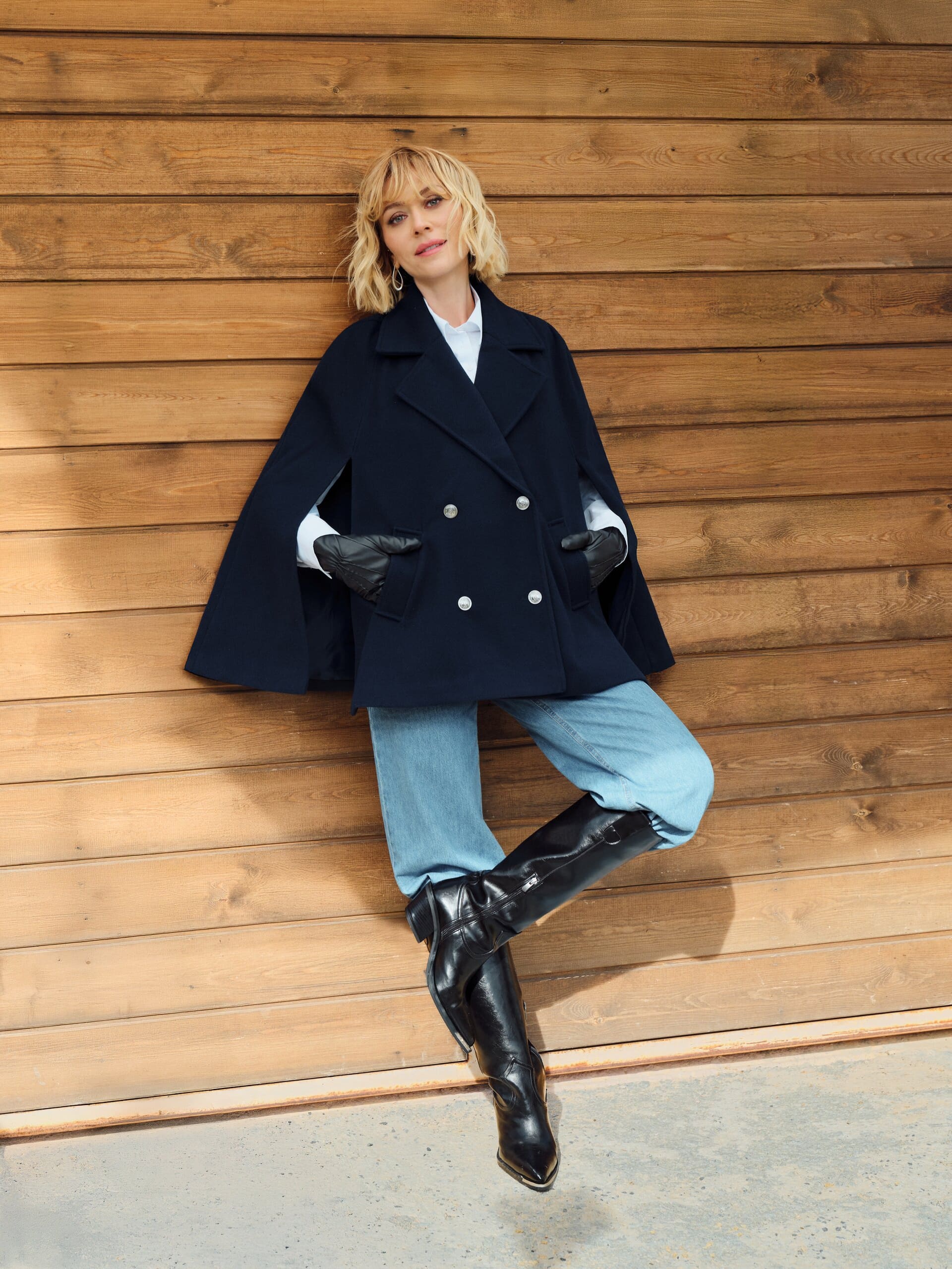Against sun-warmed timber cladding, Hazal Türesan slips leather-gloved hands into the pockets of LC Waikiki's cape-sleeve pea coat, one boot kicked up.