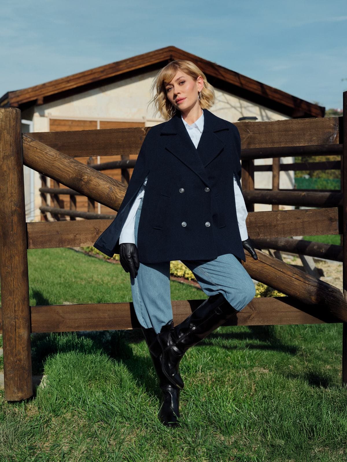 Hazal Türesan squares up to the camera at a ranch fence in LC Waikiki's navy caped pea coat, leather gloves and tall black riding boots.