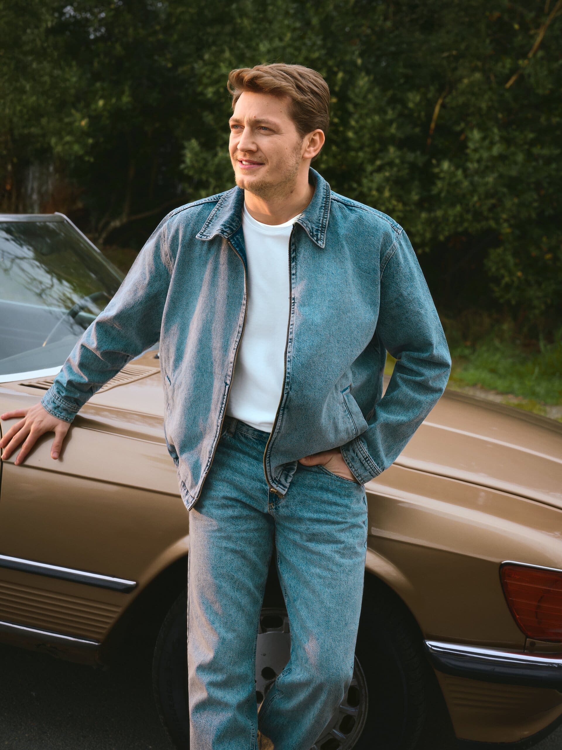 Erdem Şanlı leans on the hood of a beige classic Mercedes in a matched denim jacket and jeans for LC Waikiki.