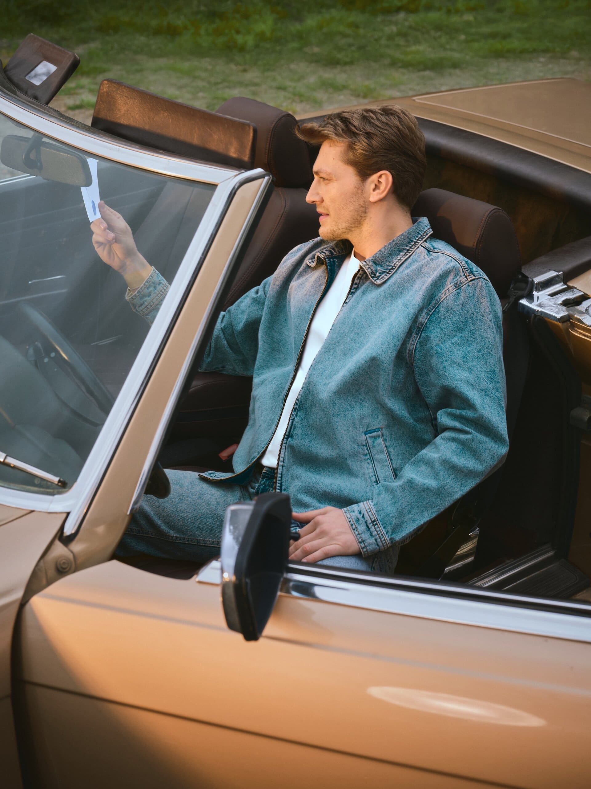 Seen in profile, Erdem Şanlı reaches for the envelope tucked at the windshield of the open-top convertible for LC Waikiki.