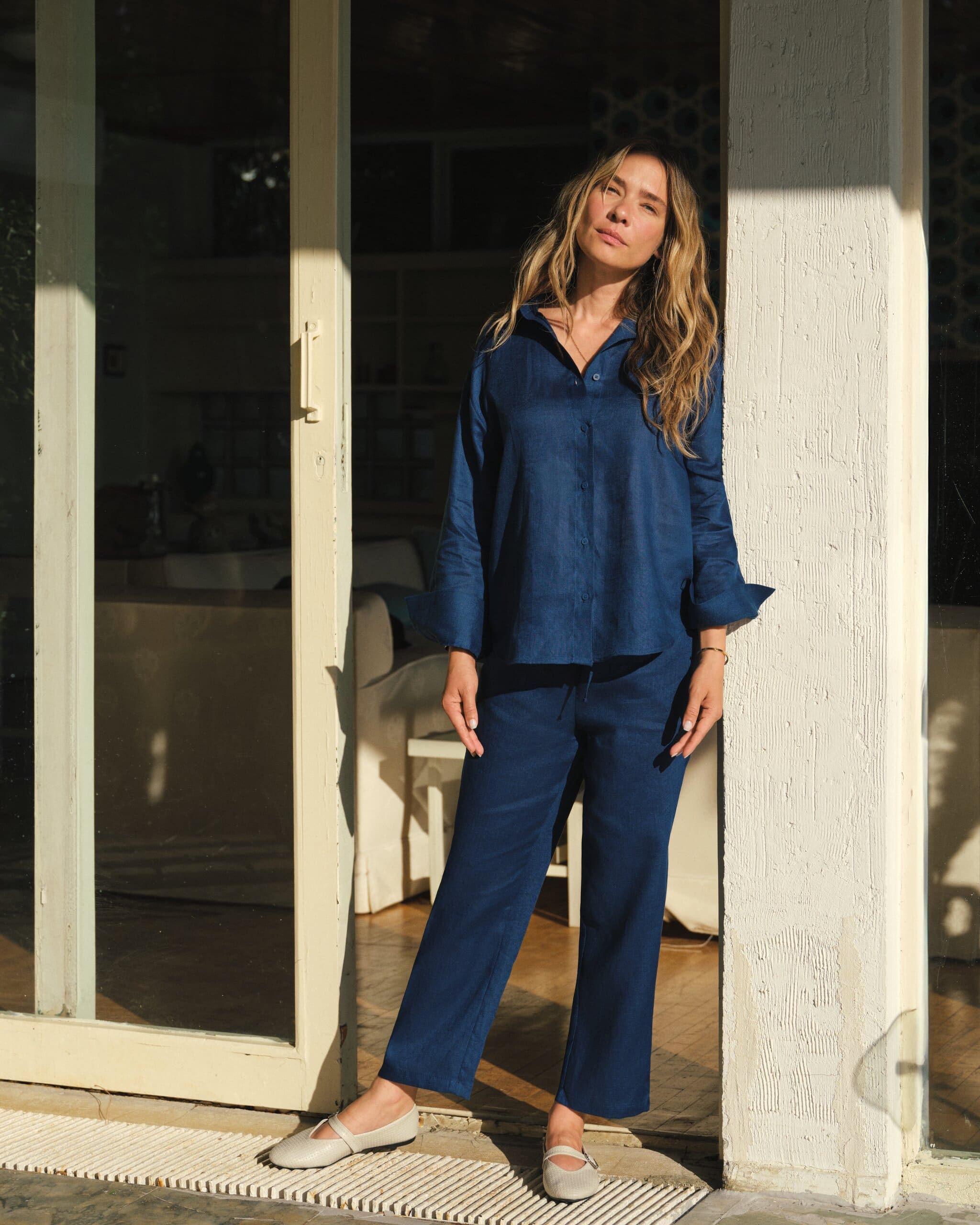 Müge Boz stands framed in a sunlit doorway in her navy linen set, cream mary-janes on the cool stone for LC Waikiki.