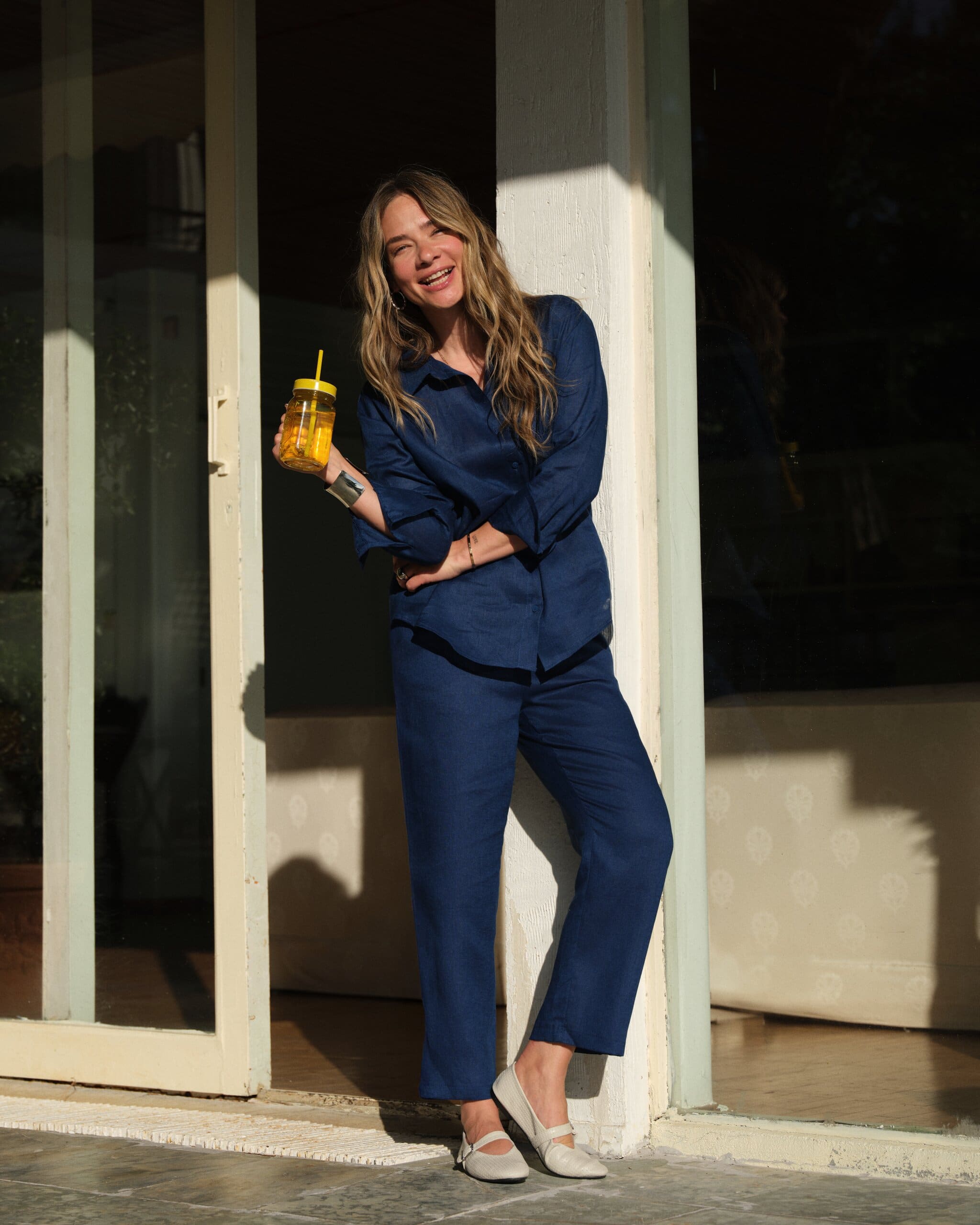 Müge Boz laughs in a navy linen set, yellow lemonade jar in hand, leaning into a sunlit doorway for LC Waikiki