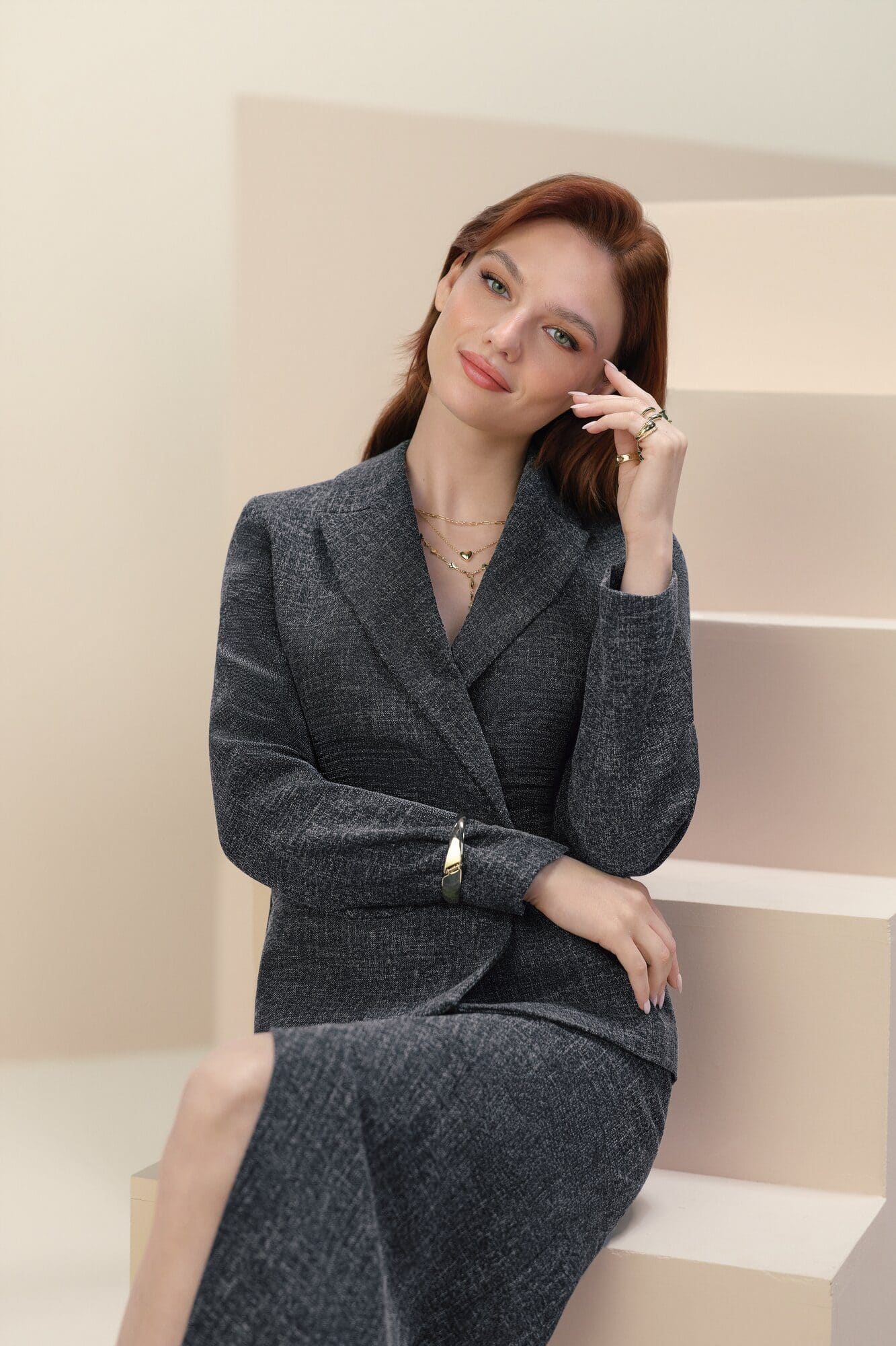 Nilsu Berfin Aktaş in a charcoal tweed suit and layered gold jewellery, seated on a blush studio staircase for LC Waikiki.