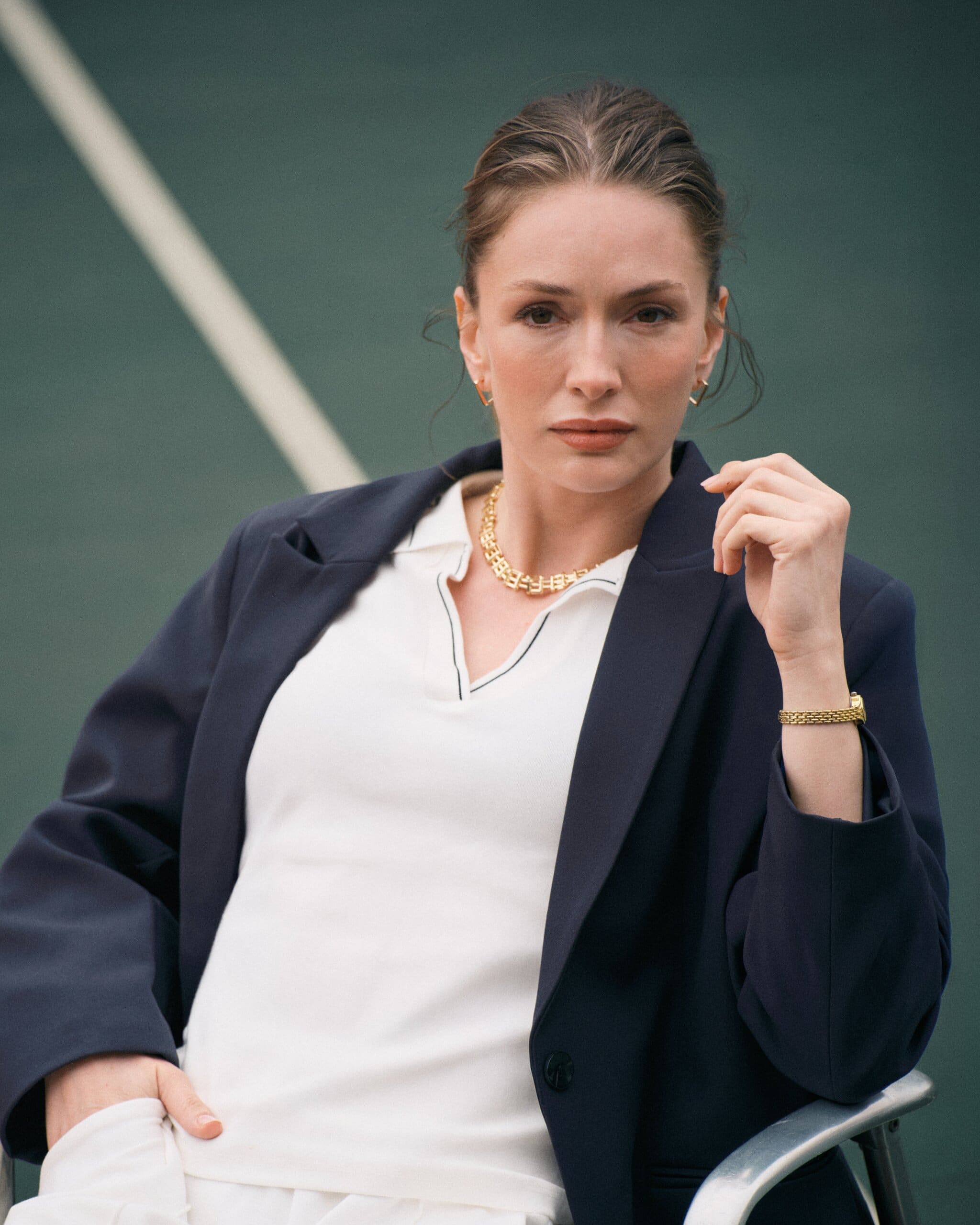 Close portrait of Yasemin Kay Allen with slicked-back hair, gold chain necklace and a navy blazer over courtside whites for LC Waikiki.