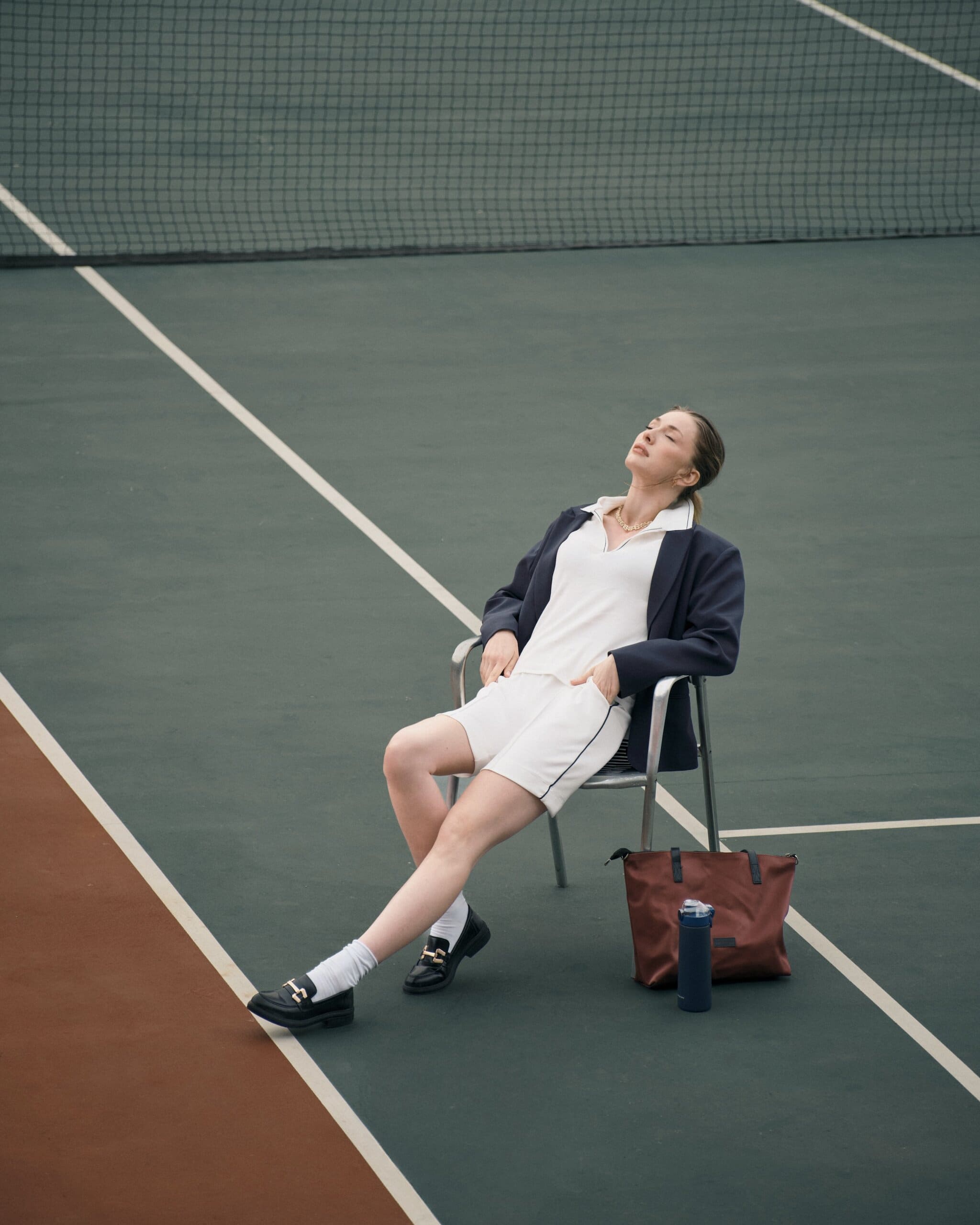 Head tipped back and eyes closed, Yasemin Kay Allen stretches out on a courtside chair in a blazer and tennis whites for LC Waikiki.