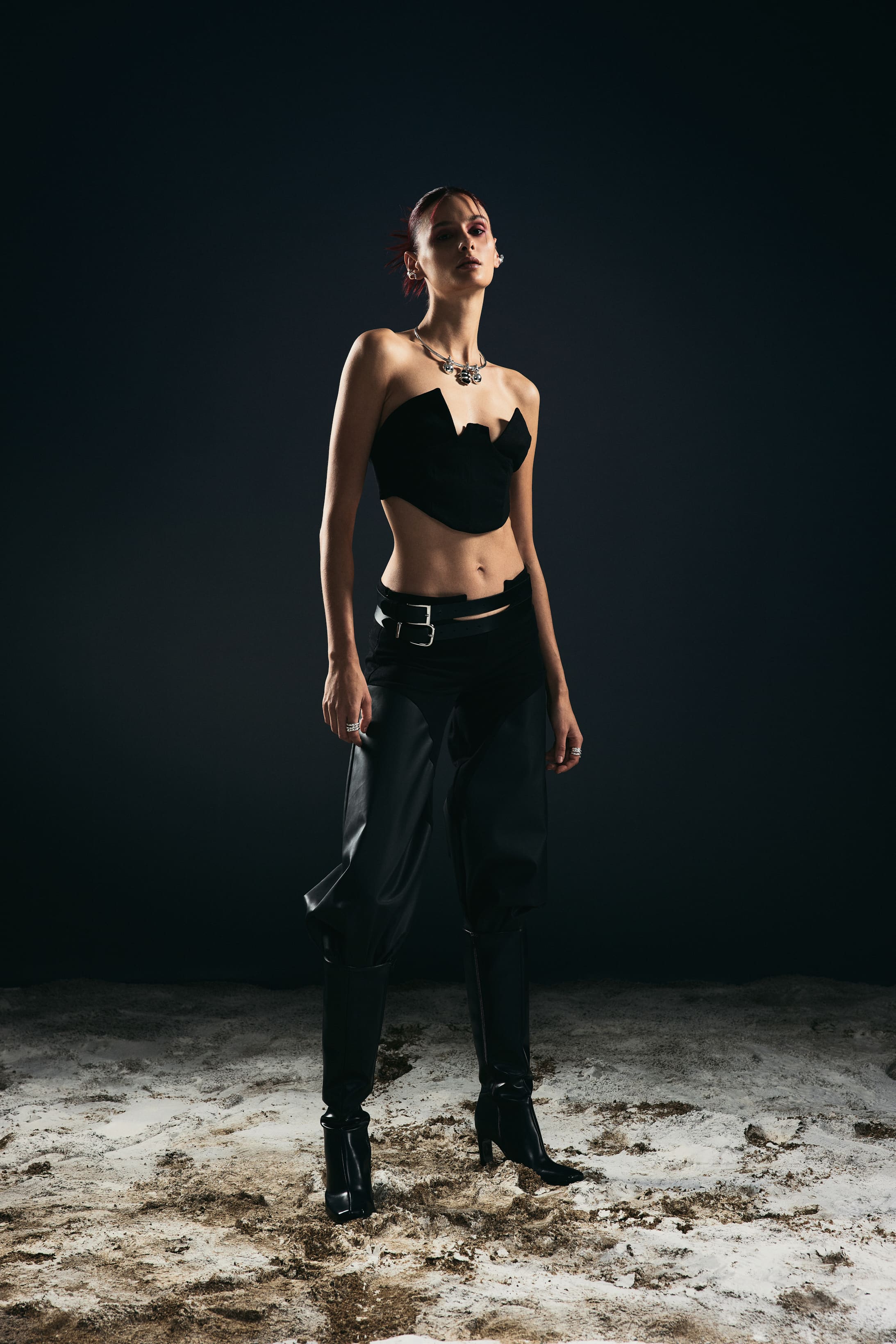 The sweetheart bustier drops to double-belted leather trousers and knee boots in a full-length Mysamoon look on the sand.