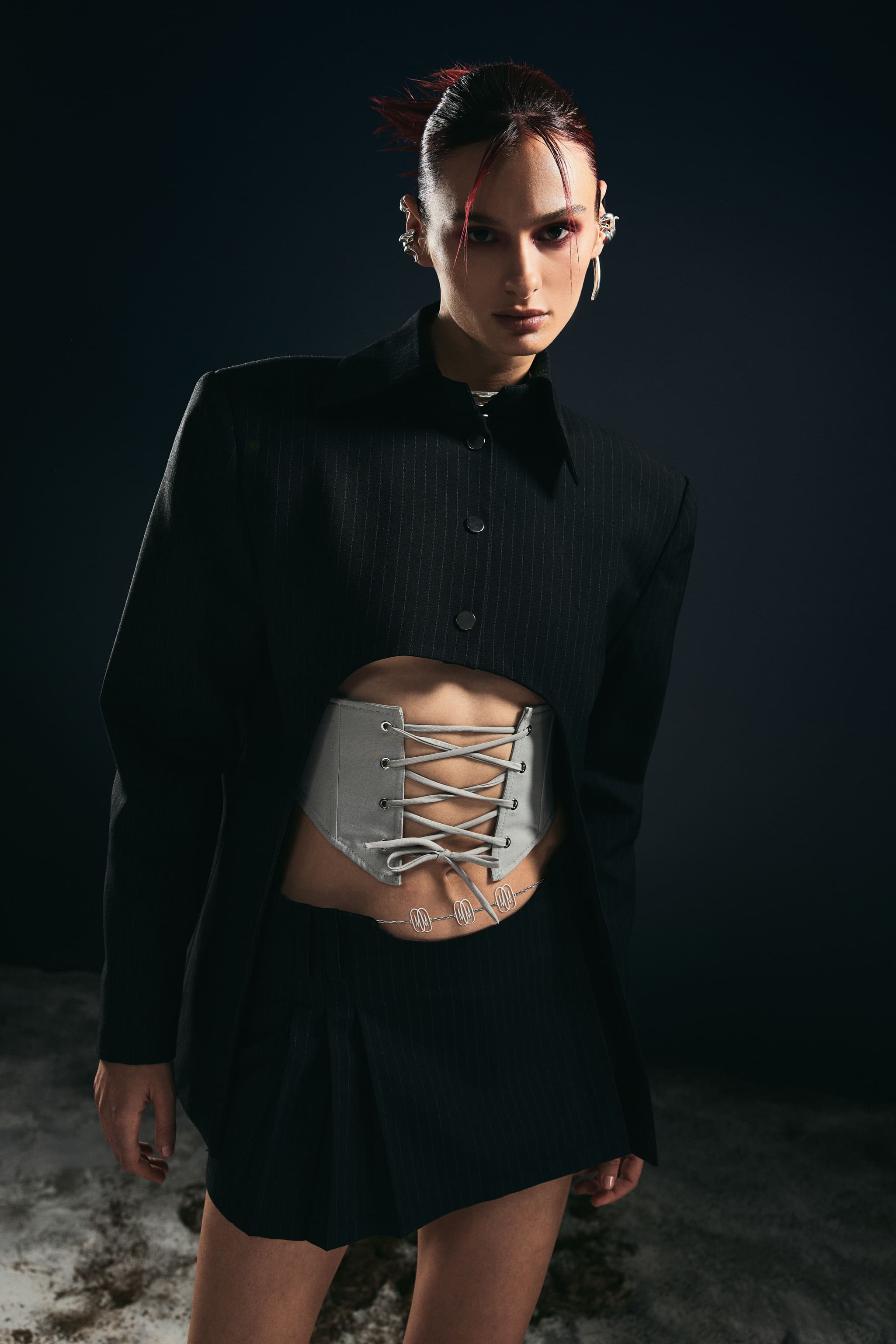 A cropped pinstripe blazer laced with a grey corset belt, worn with crimson-shadowed eyes for Mysamoon.