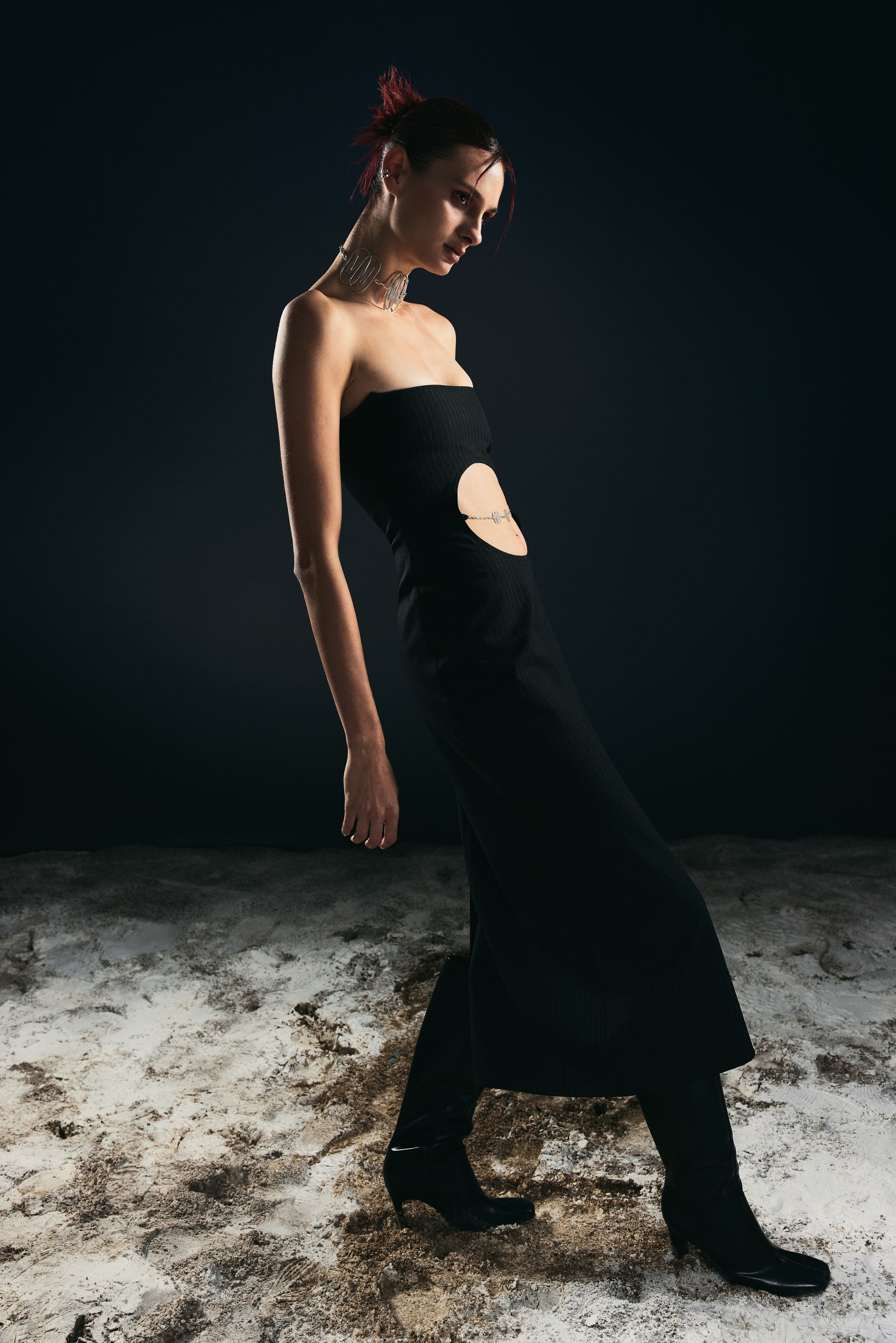 In profile, a strapless pinstripe column with an oval waist cutout draws one long line across Mysamoon's sand-strewn set.