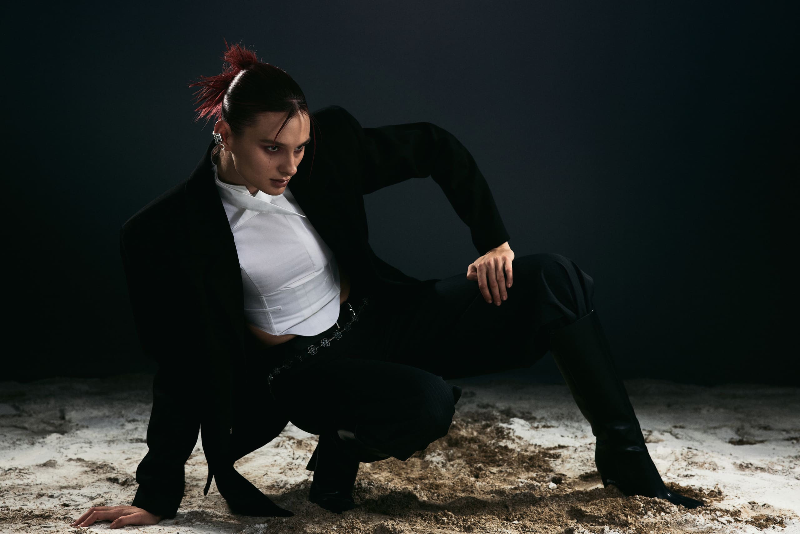 Crouched low on churned sand in an oversized blazer and white corset top, the closing frame of the Mysamoon campaign.
