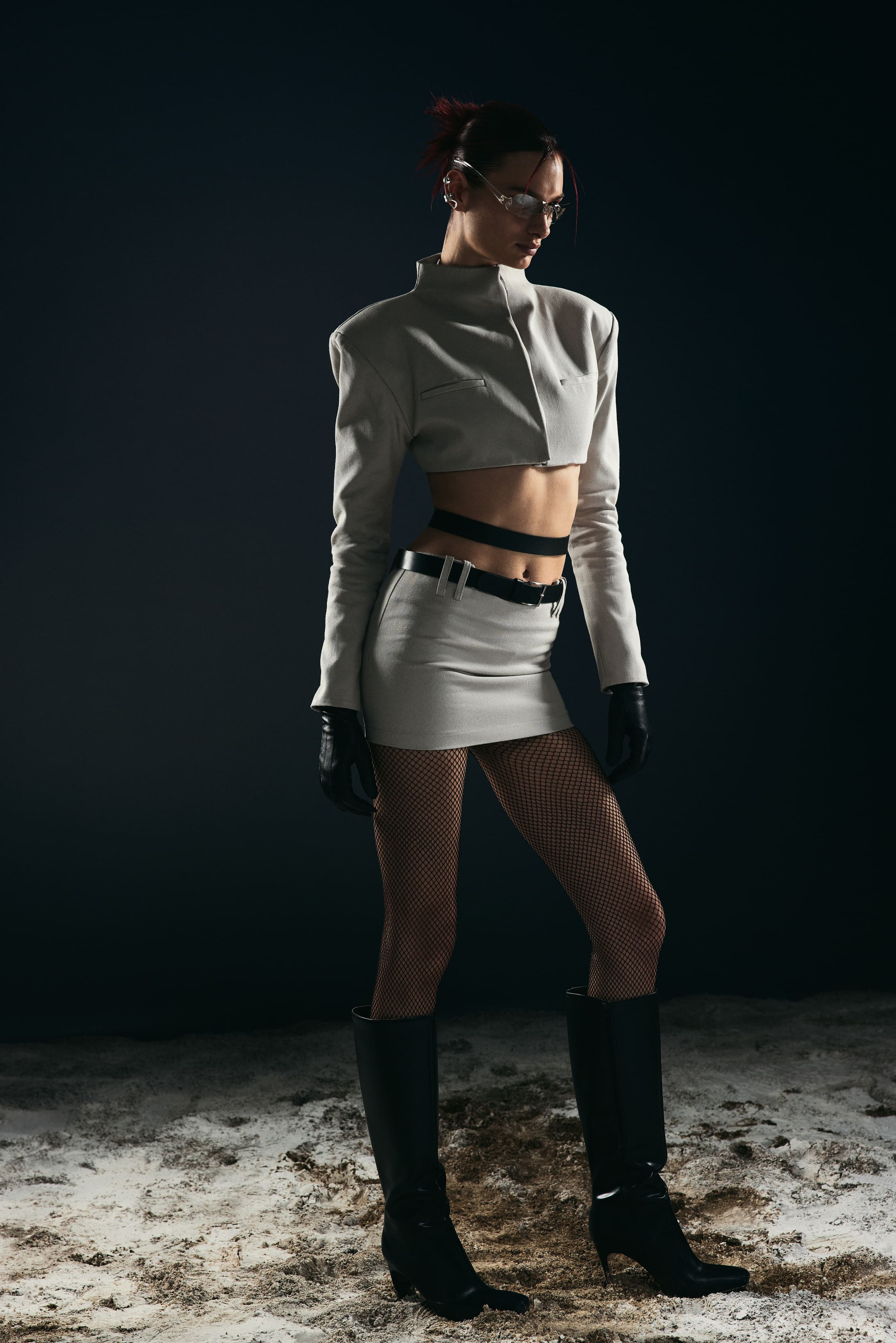 Turned in profile, the stone-grey jacket and mini skirt run down through fishnets to knee-high boots for Mysamoon.
