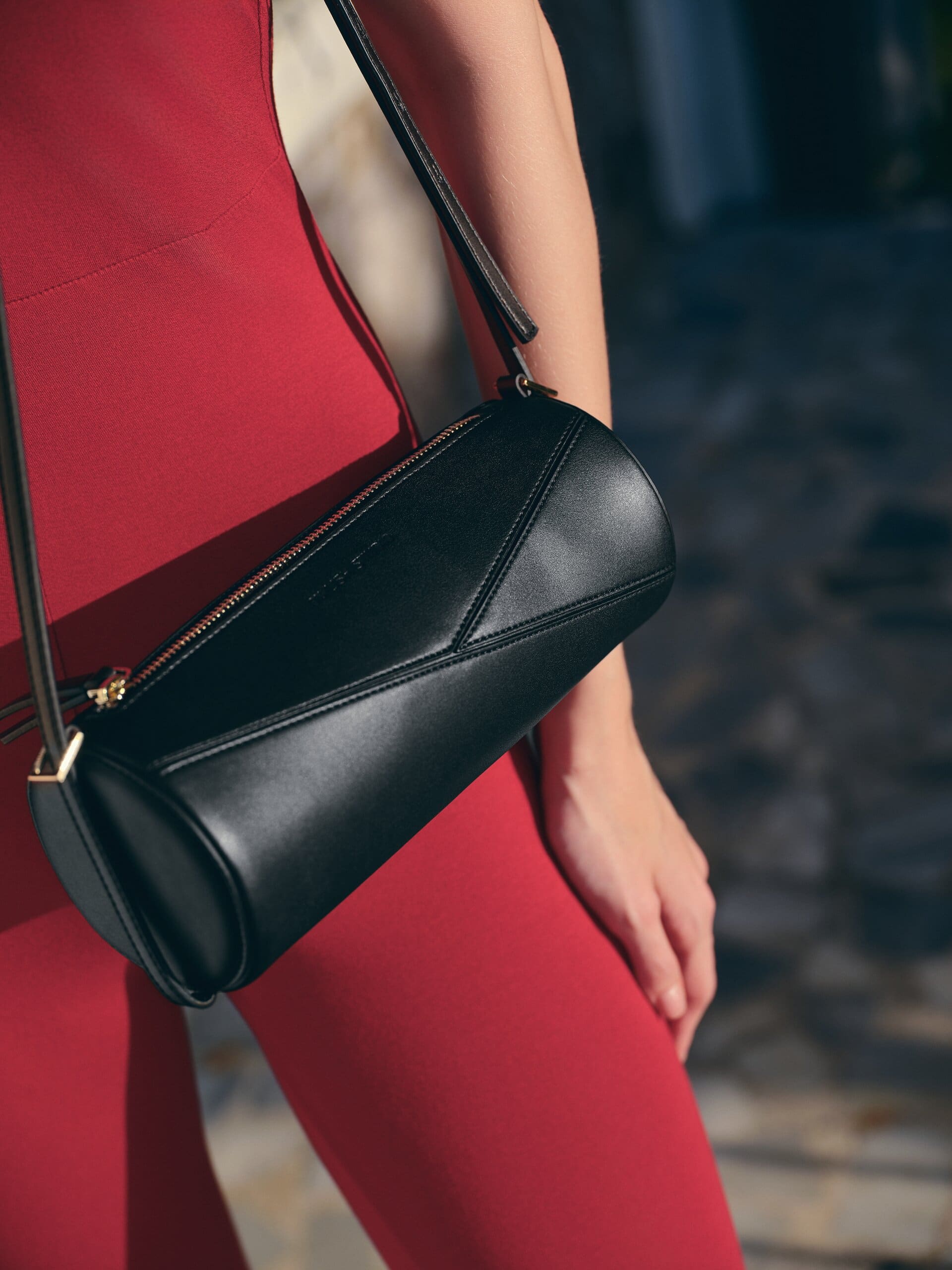 Close on the black leather barrel bag and its angular seaming, worn at the hip of the wine-red catsuit for Owlish Studio.