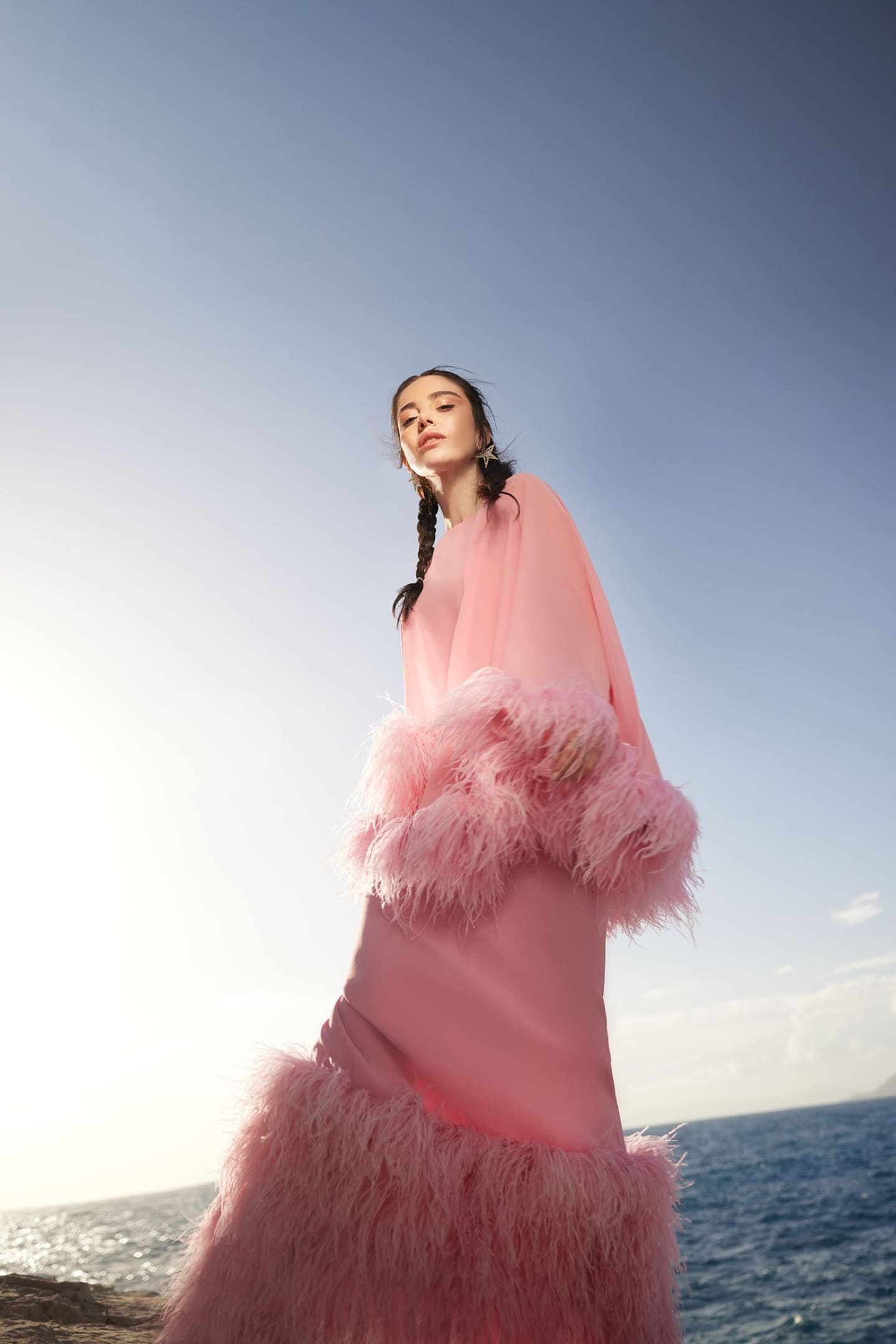 Özgecan Gürel in a pink feather-trimmed gown shot from below against open sky and sea for Cover Story