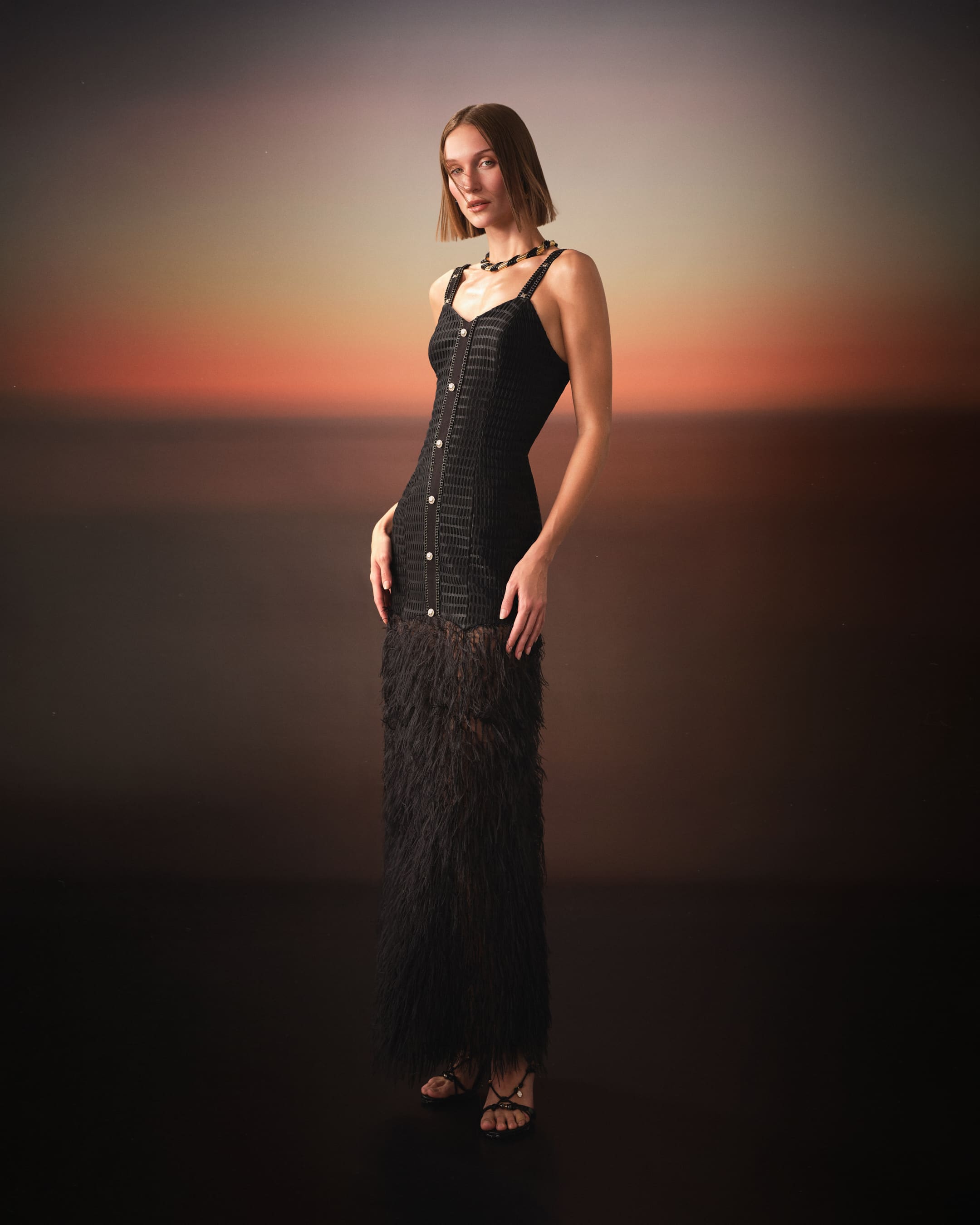 A chain-trimmed column dress dissolving into ostrich feathers at dusk for Saint Ones.