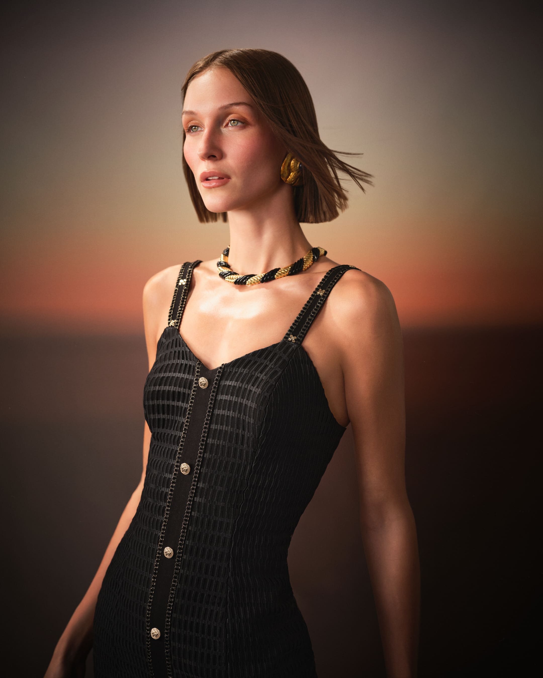 Twisted gold-and-black jewellery over the chain-trim bodice, glowing in twilight for Saint Ones.