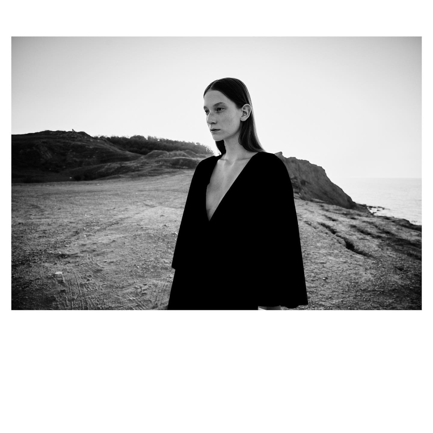A plunging black cape dress on a windswept coastal headland opens ST Studio's Unborn campaign.