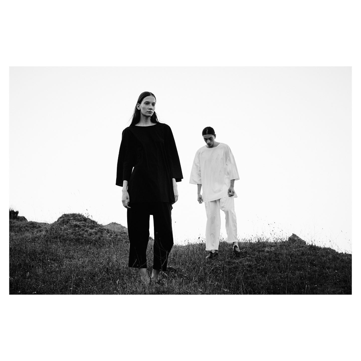 Two models in oversized black and white tunics descend a wild hillside for ST Studio.