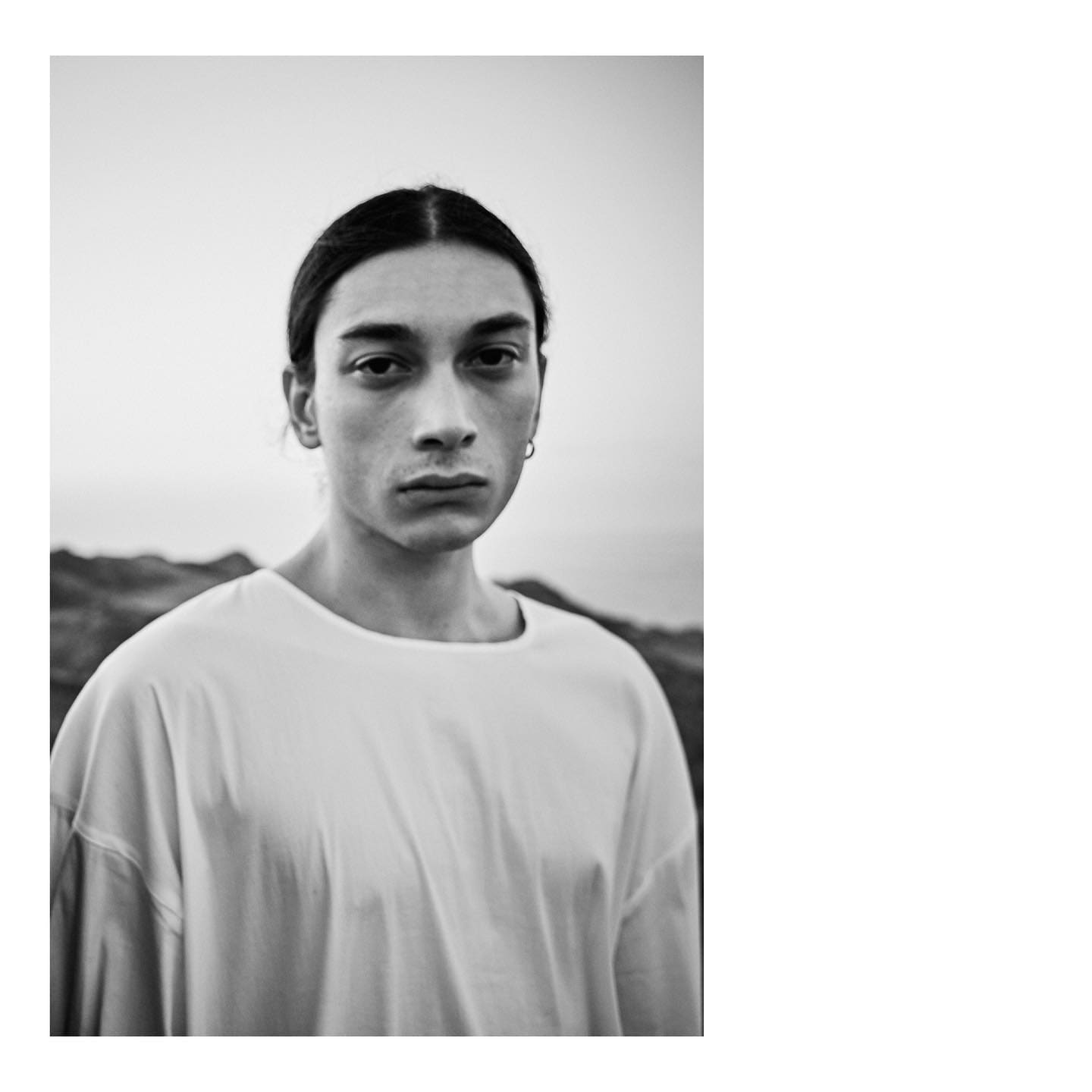 A close portrait in a collarless white tee against a fading coastal horizon for ST Studio.