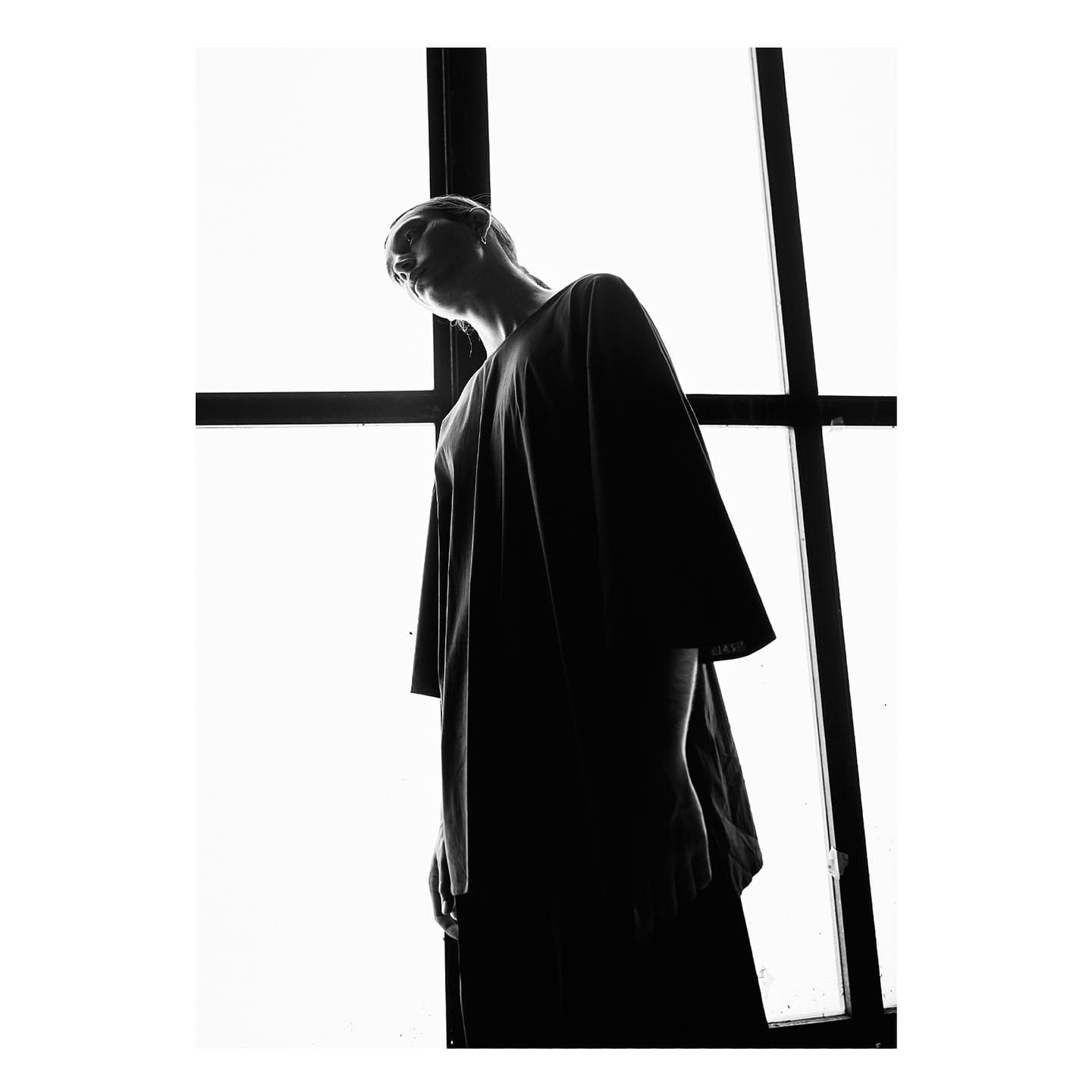 An oversized black tee reduced to silhouette against a gridded studio window for ST Studio.