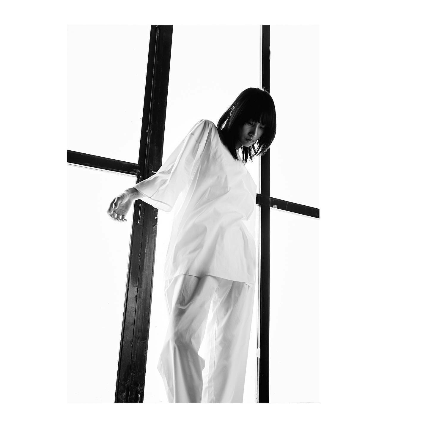 Caught mid-turn at the factory glazing, ST Studio's sheer white tunic drifts with the model's downward glance.