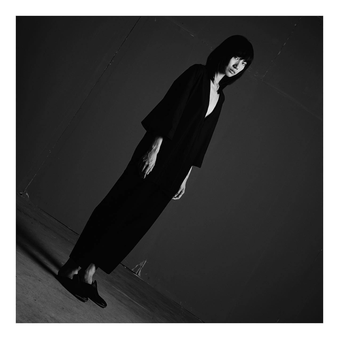 Tilted into near-darkness, the bangs-framed face above ST Studio's long black tunic barely surfaces from shadow.