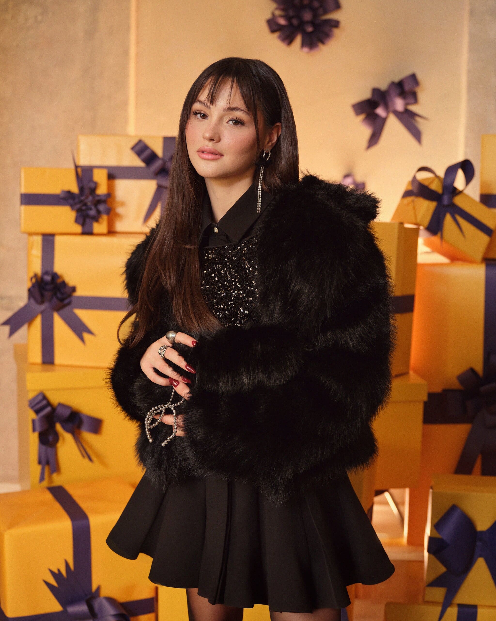 Derya Pınar Ak pulls the faux-fur collar close, a beaded bow charm laced through her fingers under the amber party light for XSIDE.