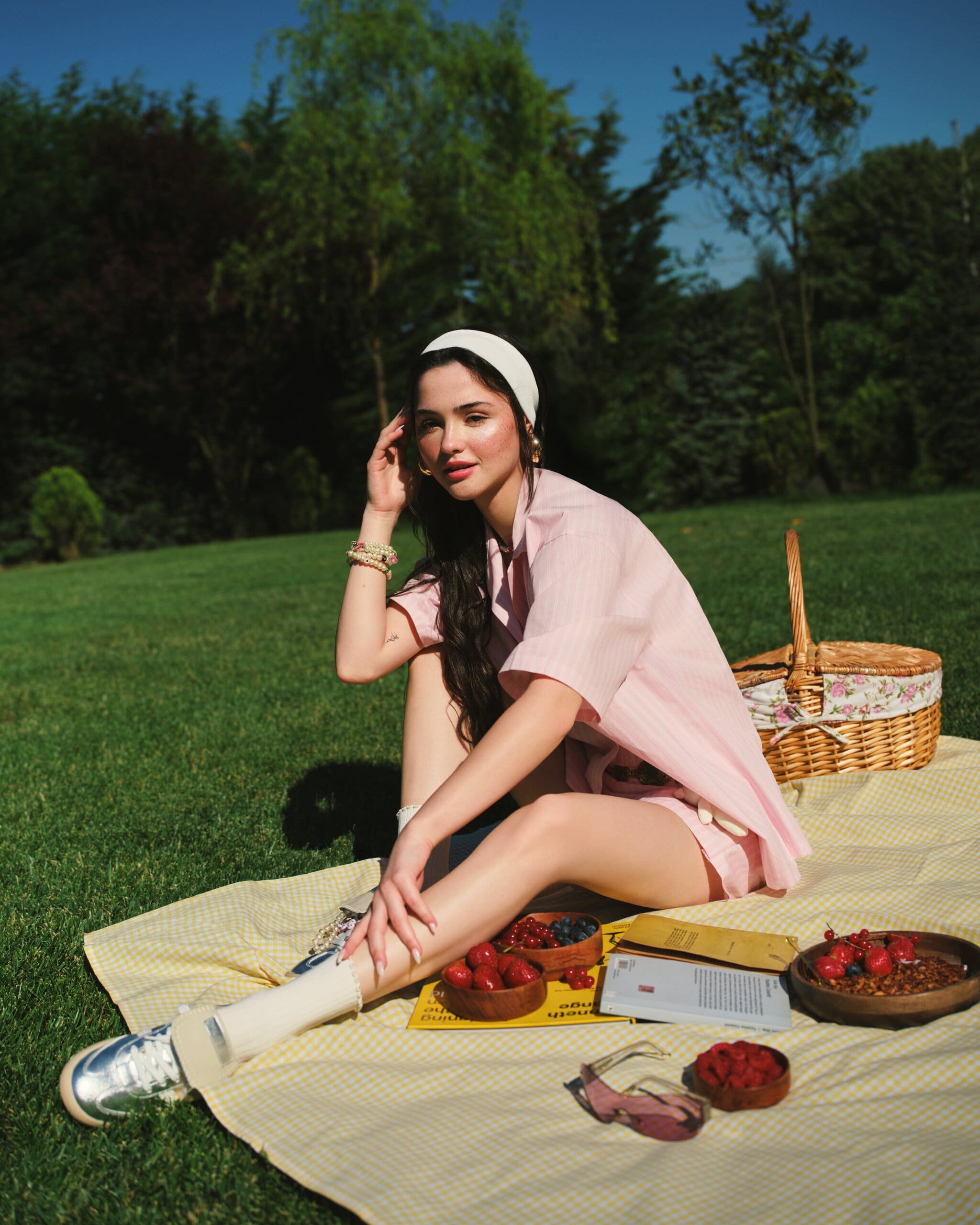 Derya Pınar Ak in a pale pink striped co-ord and cream headband, seated on a yellow gingham picnic blanket with berries and a wicker basket for XSIDE.