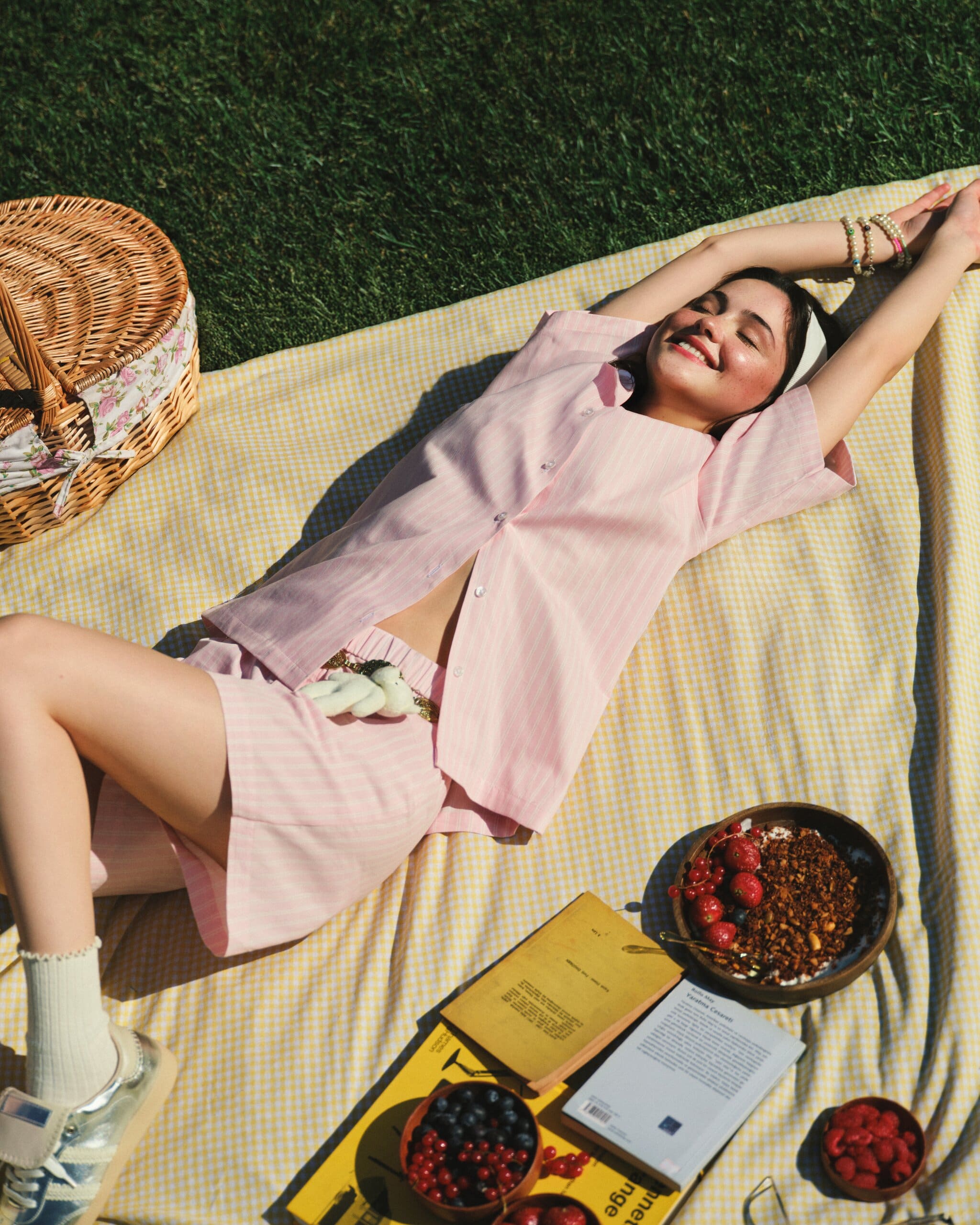 Derya Pınar Ak stretches out laughing on a yellow gingham blanket, shot from above in pink striped pyjama layers for XSIDE.