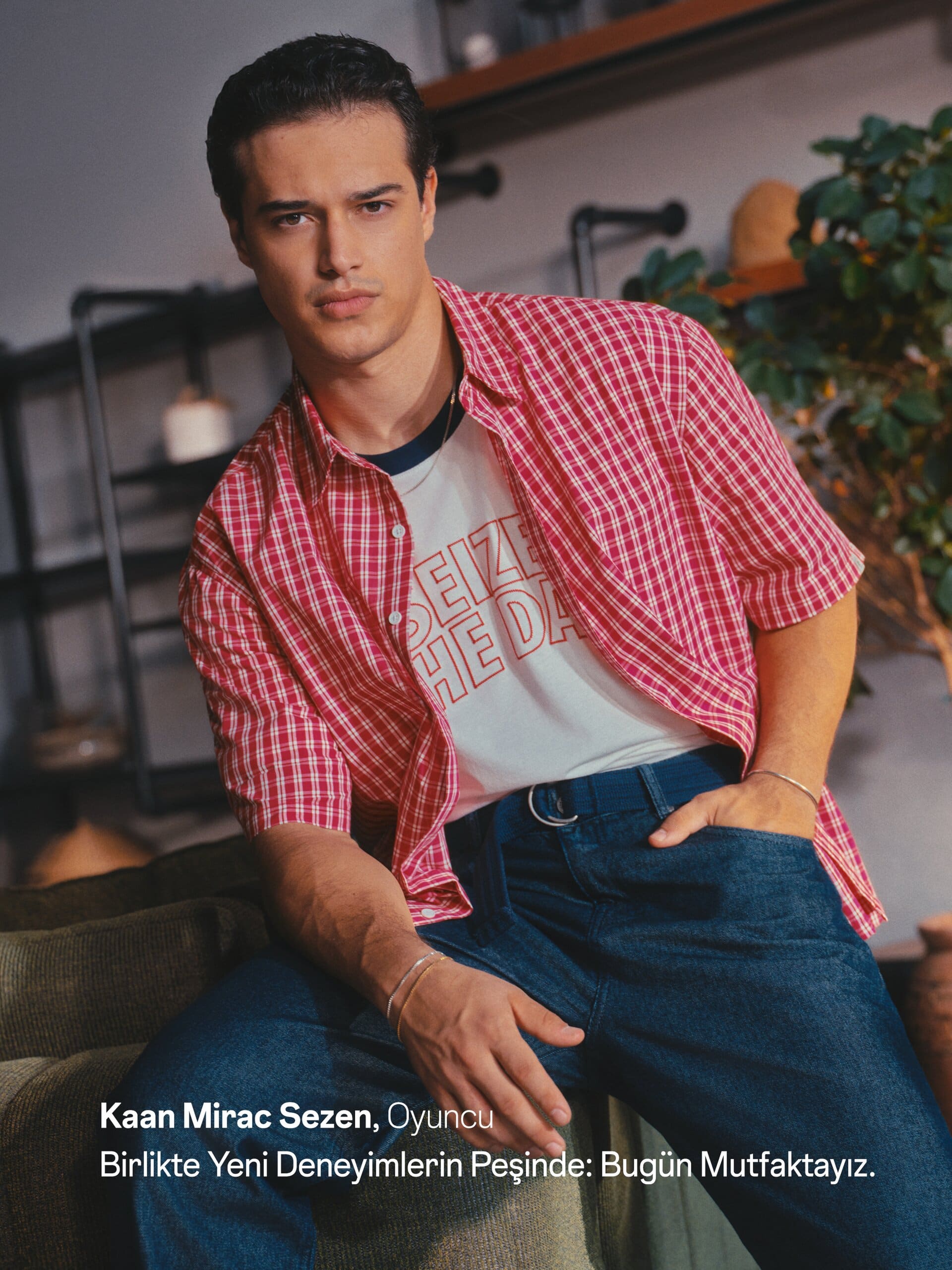 Kaan Miraç Sezen perches on a sofa arm in a red plaid overshirt and raw denim for XSIDE.