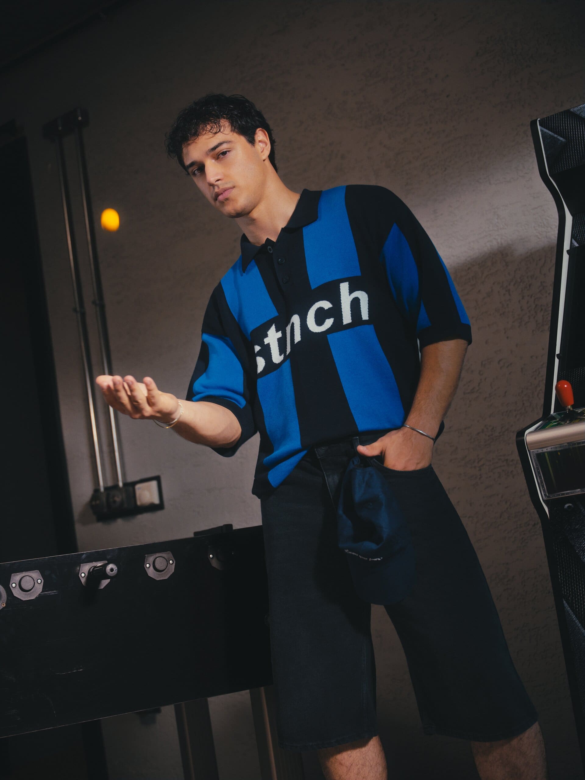 Kaan Miraç Sezen flips a foosball into the air in a striped knit polo in the games room for XSIDE.