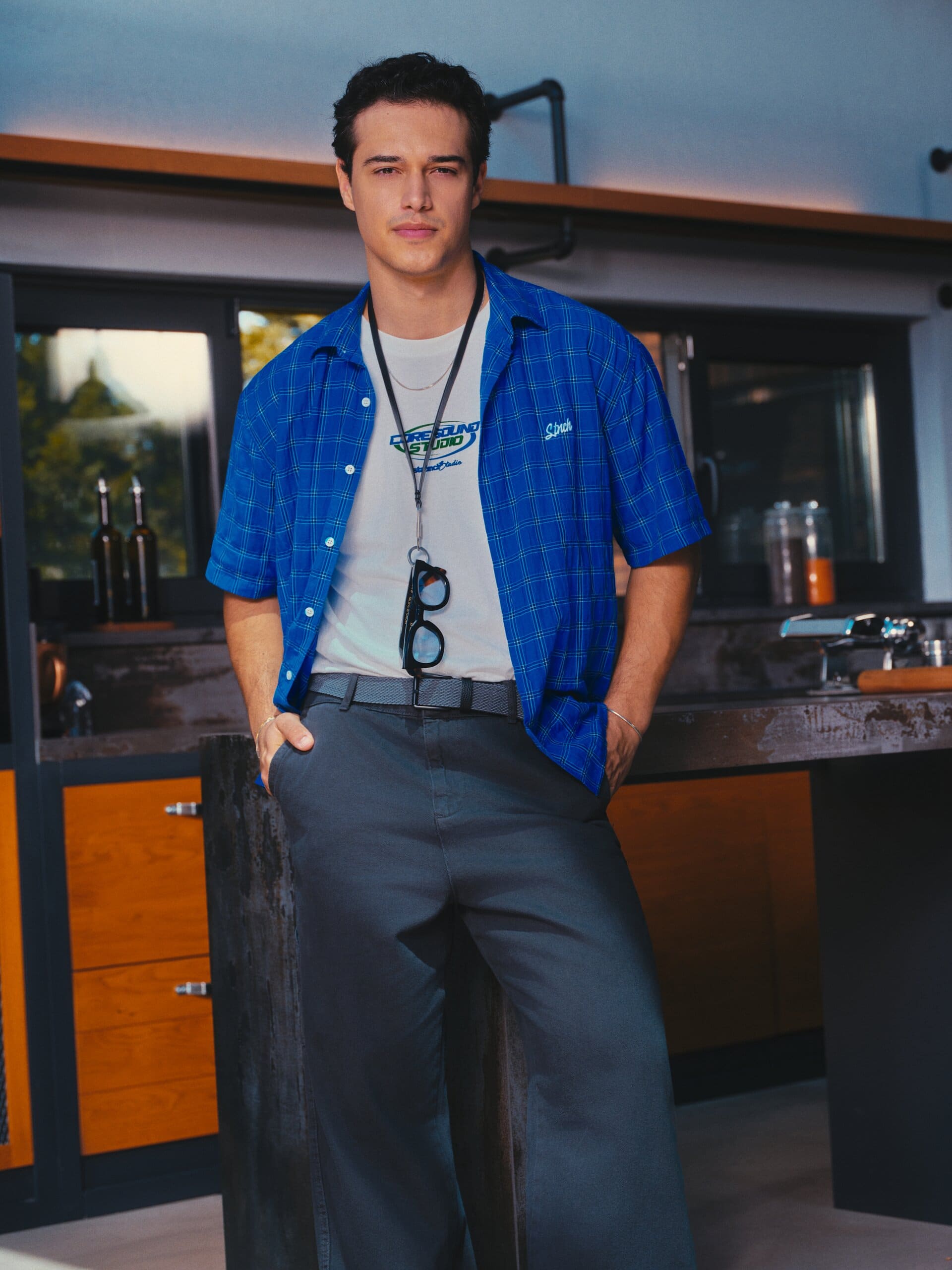 Kaan Miraç Sezen stands hands-in-pockets in the dusk-lit kitchen, glasses slung from a lanyard, for XSIDE.