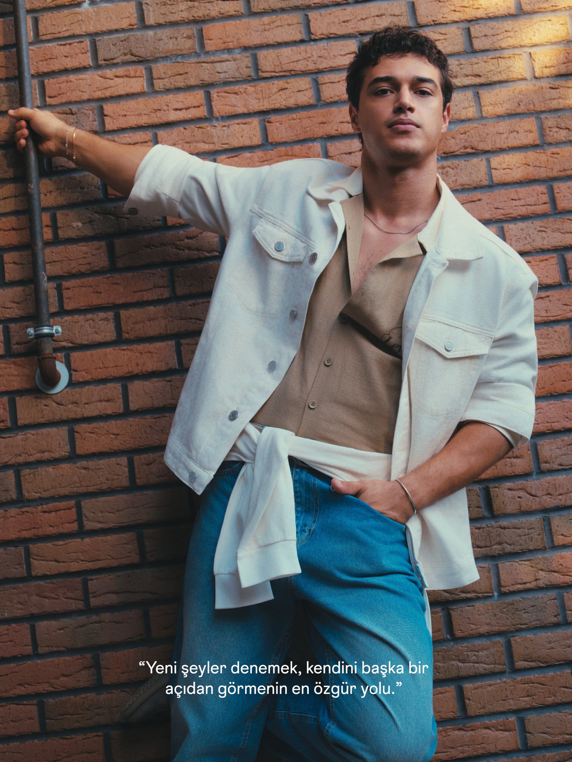 Kaan Miraç Sezen stretches an arm along a brick wall in an ecru overshirt and light-wash jeans for XSIDE.